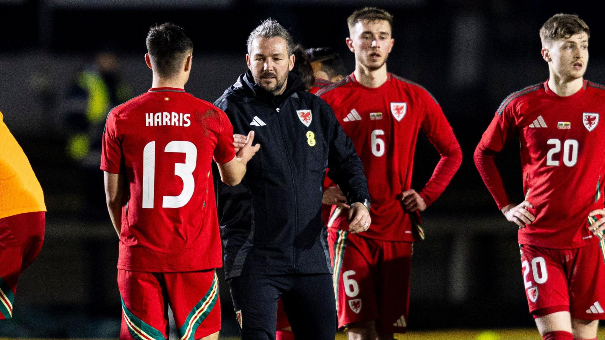 Wales Under-21 manager Matty Jones shakes hands with Luke Harris (back to camera) while other players walk nearby