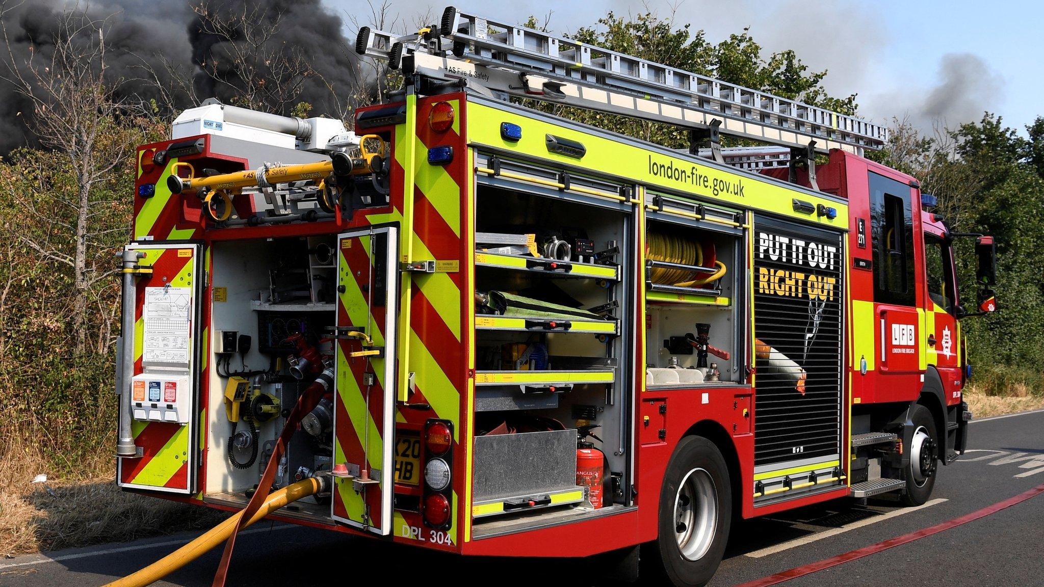 A fire truck parked near a fire that burns during a heatwave, in east London