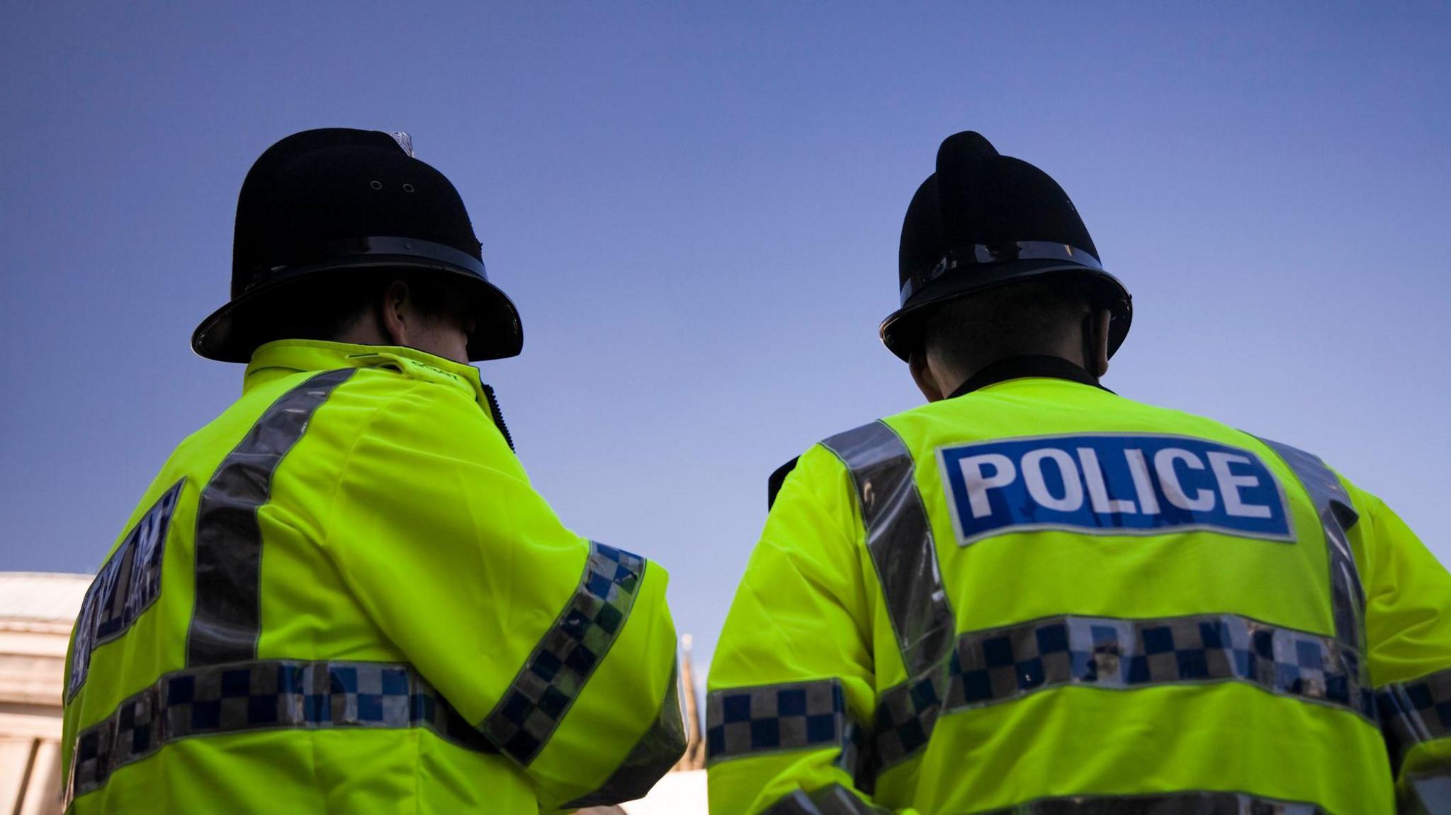 Two British Policemen wearing Traditional Helmets.