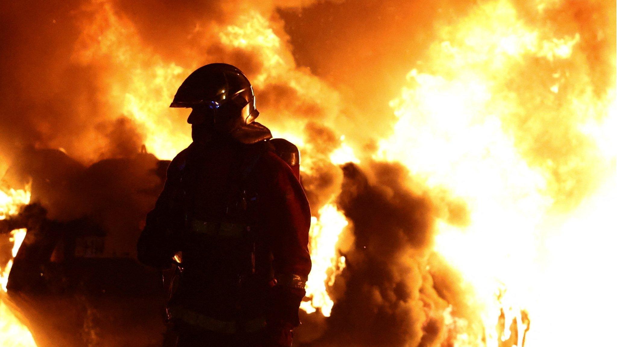 Firefighter standing in front of a burning vehicle during clashes between protesters and police in Nanterre, near Paris, on 28 June