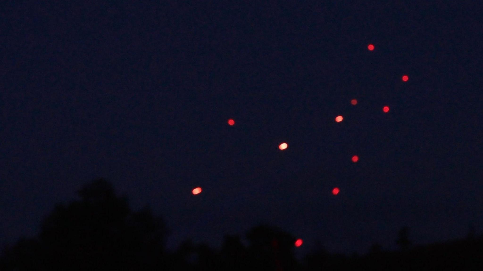 Tracer fire - which looks like eleven small red dots - can be seen amongst pitch black sky. Tree tops are just about visible in the darkness.