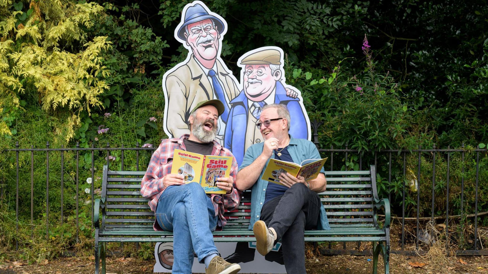 Greg Hemphill and Ford Kiernan both laugh as they look over a new Still Game comic book 