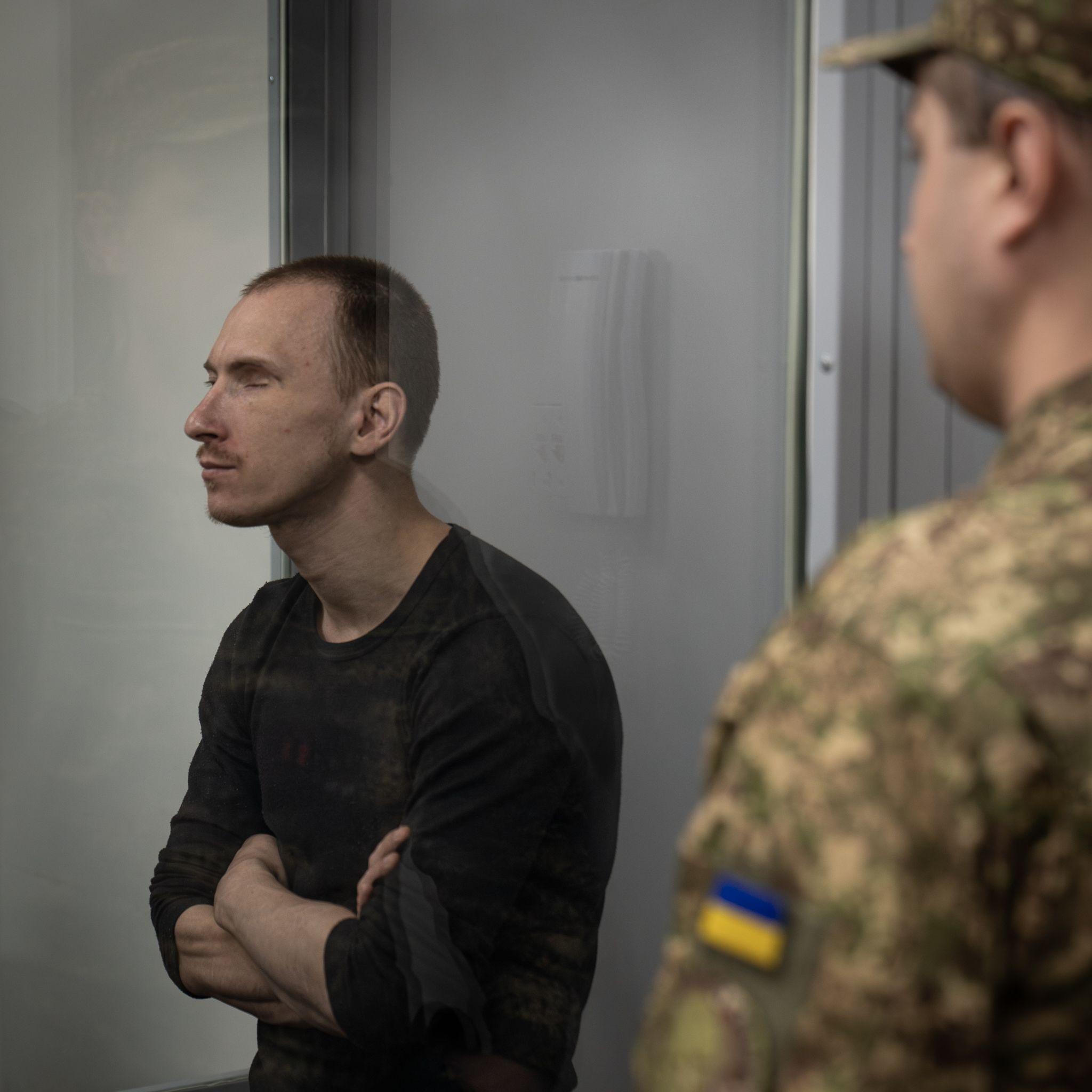Dmitriy Kurashov in the dock. He has short hair and is wearing a dark long-sleeved top. Part of a Ukrainian uniform can be seen in front of him.