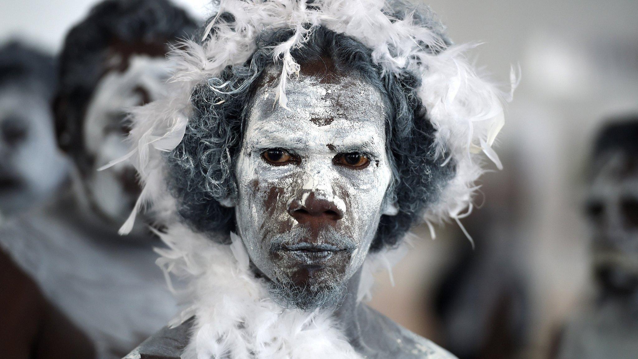 Aboriginal performers wearing traditional ceremonial costume stand together near the main entrance of Parliament House