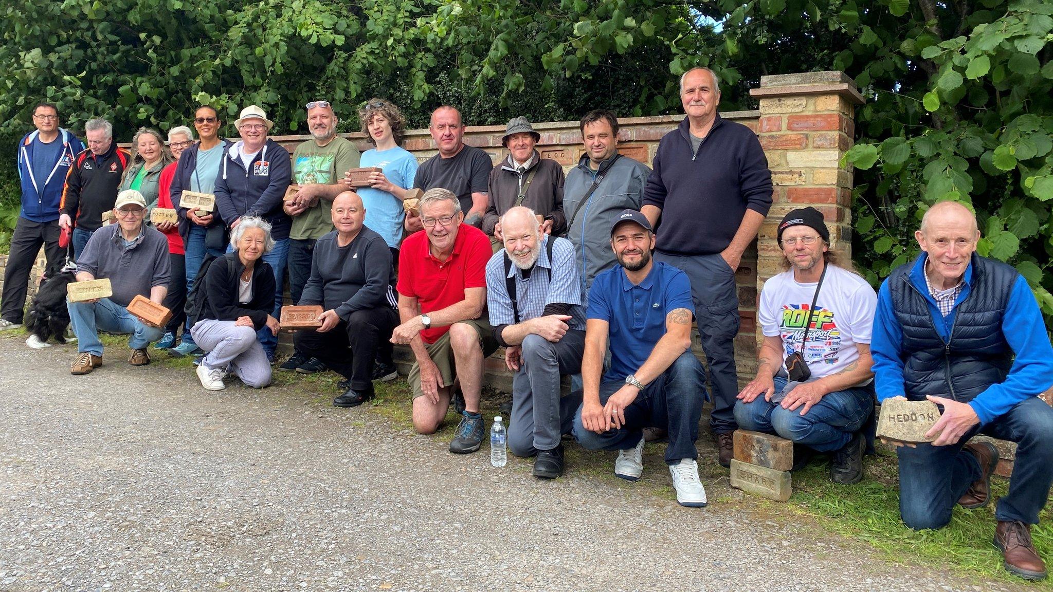 Visitors to Path Head Water Mill for a brick swap event, lined up against a wall made from old bricks