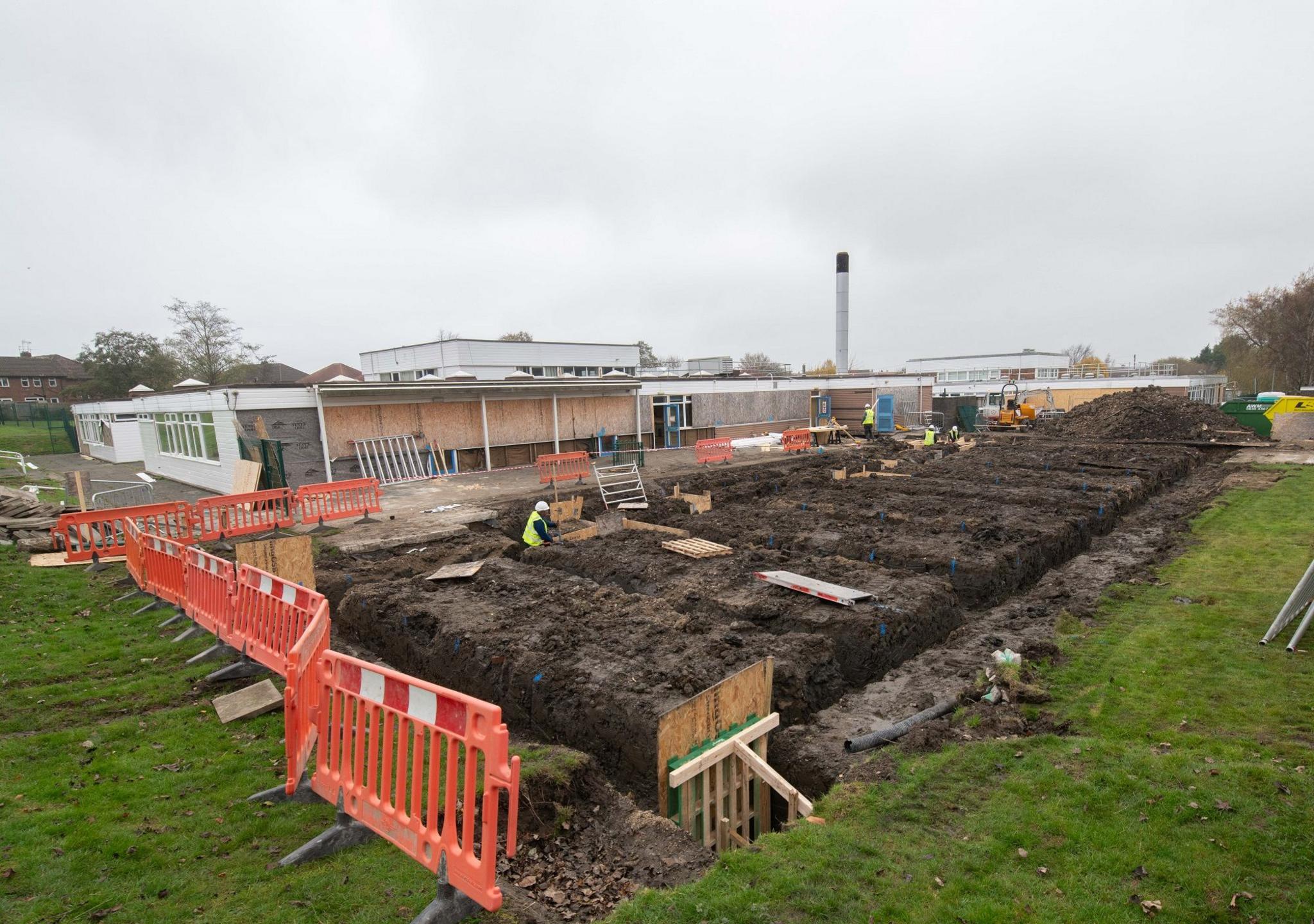 A building site with school buildings in the background and soil foundations in the foreground