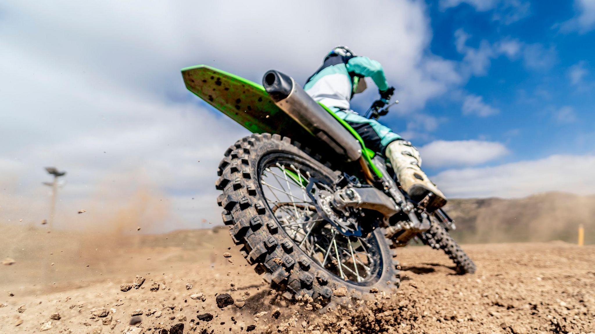 Library image of an off-road bike being ridden on a dirt trail. The back wheel is kicking up dirt. The rider is wearing a blue-and-white outfit and helmet.