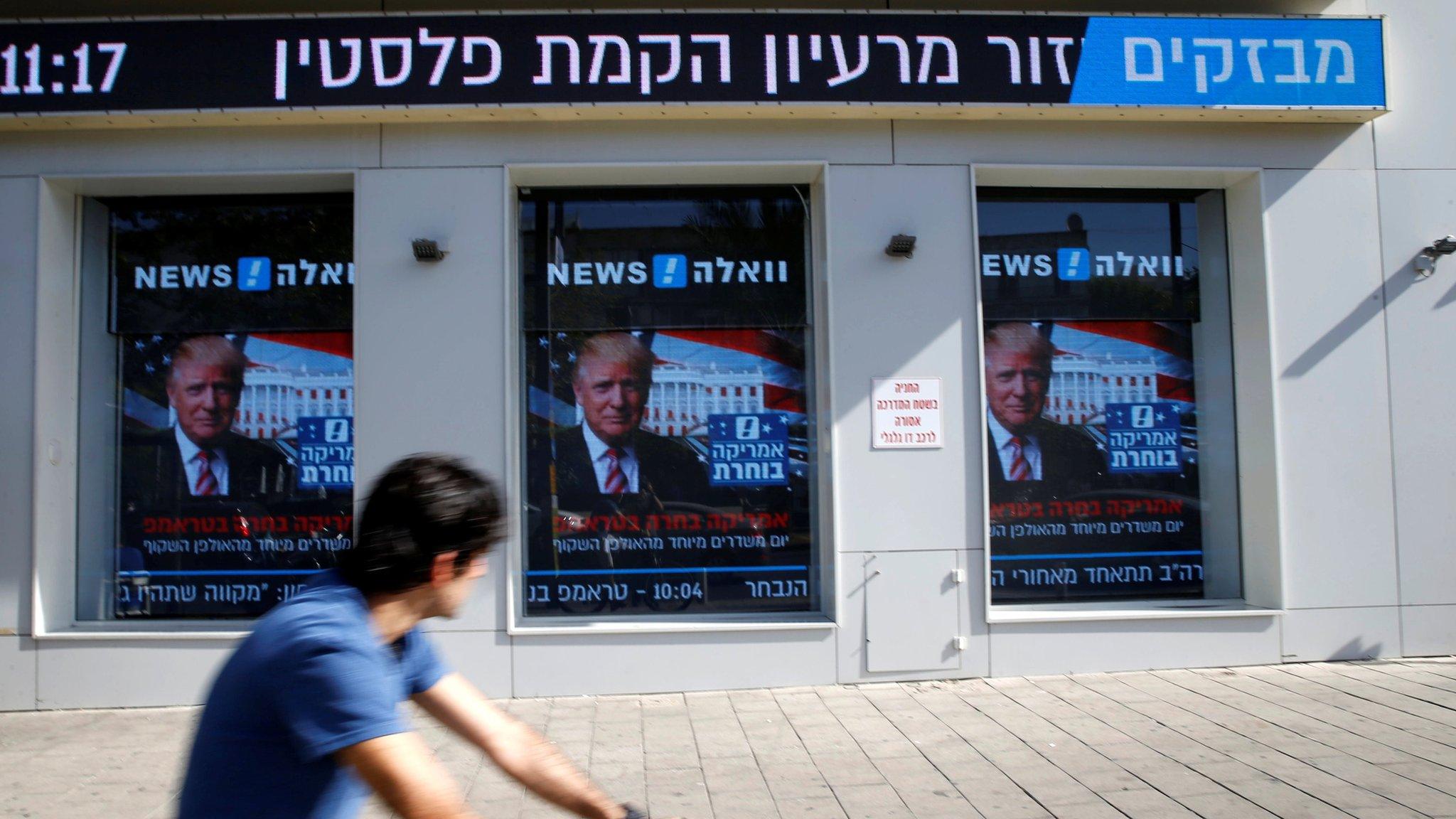 A man cycles past images of Donald Trump displayed on monitors in Tel Aviv, Israel (9 November 2016)