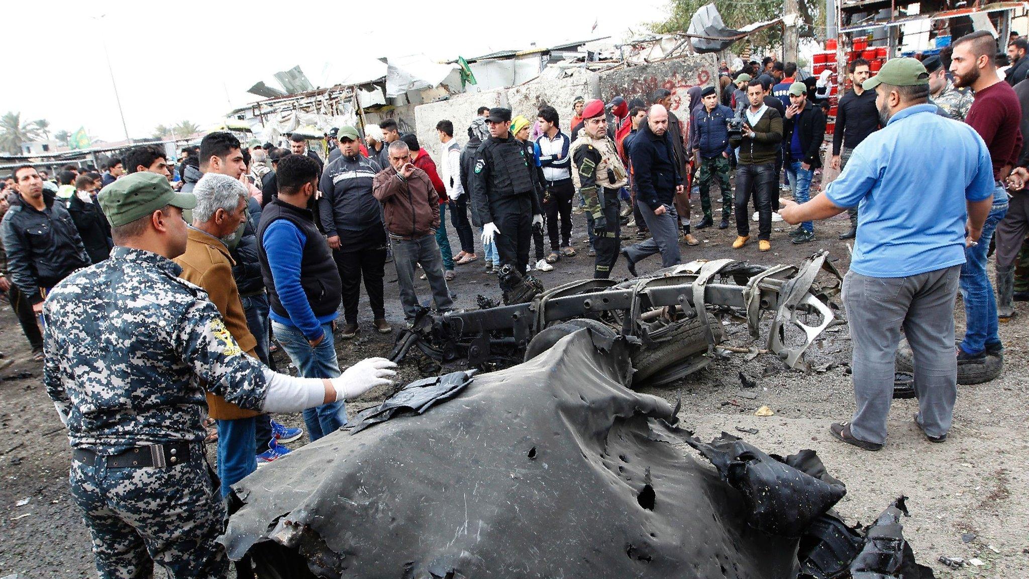 Iraqi police and bystanders look at the wreckage of a vehicle destroyed in a suicide car bomb attack in Sadr City, Baghdad (2 January 2017)