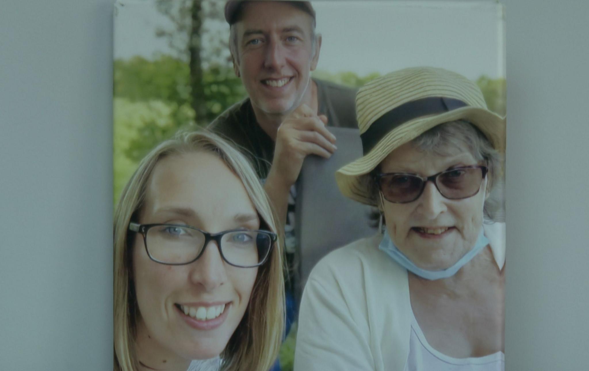 Anne Clarke wears a straw hat and sunglasses with facemask around her chin. She is with her two adult children.