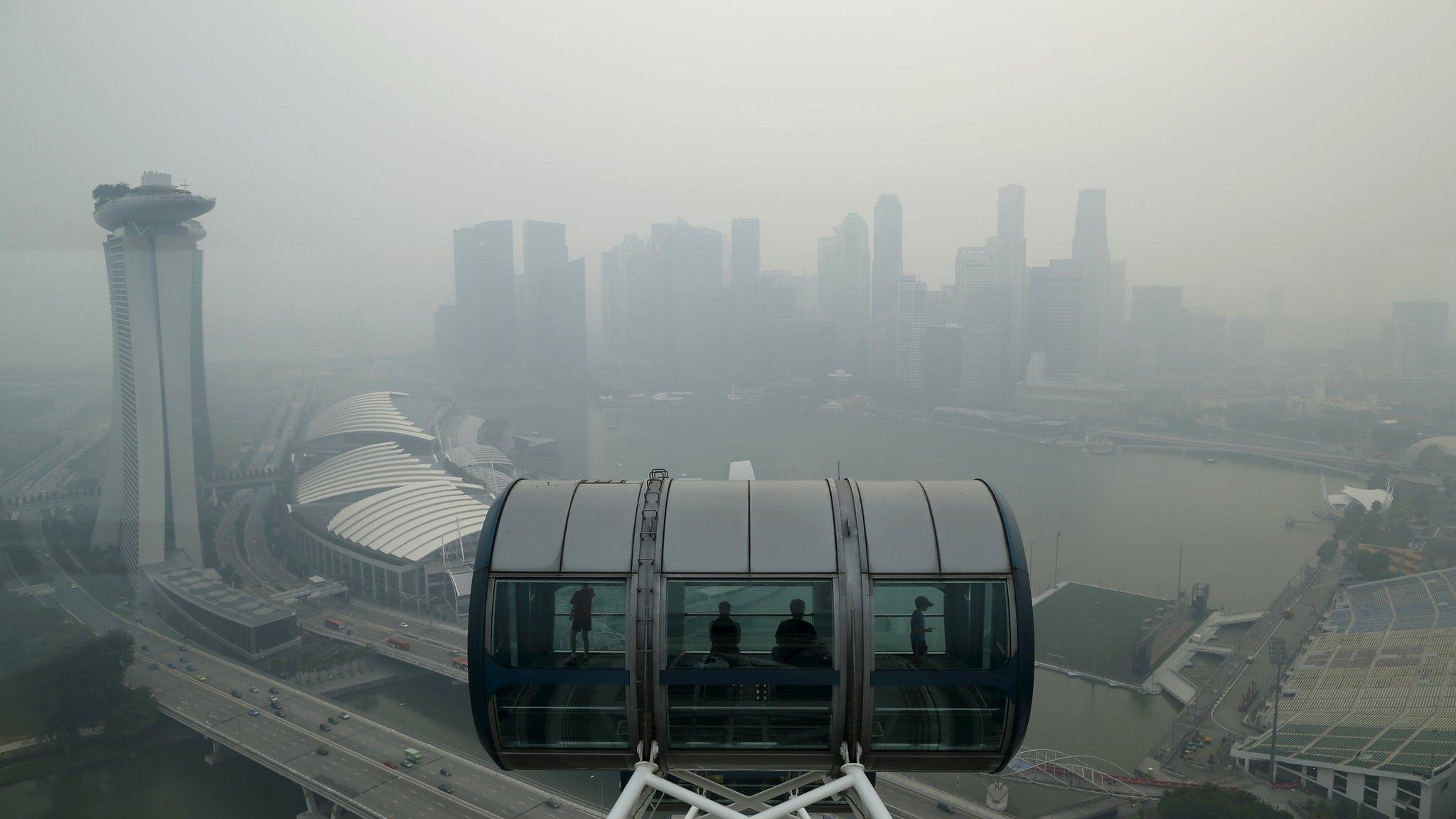 Tourists sit in a capsule on the Singapore flyer observatory wheel overlooking the skyline of the central business shrouded by haze in Singapore September 10, 2015