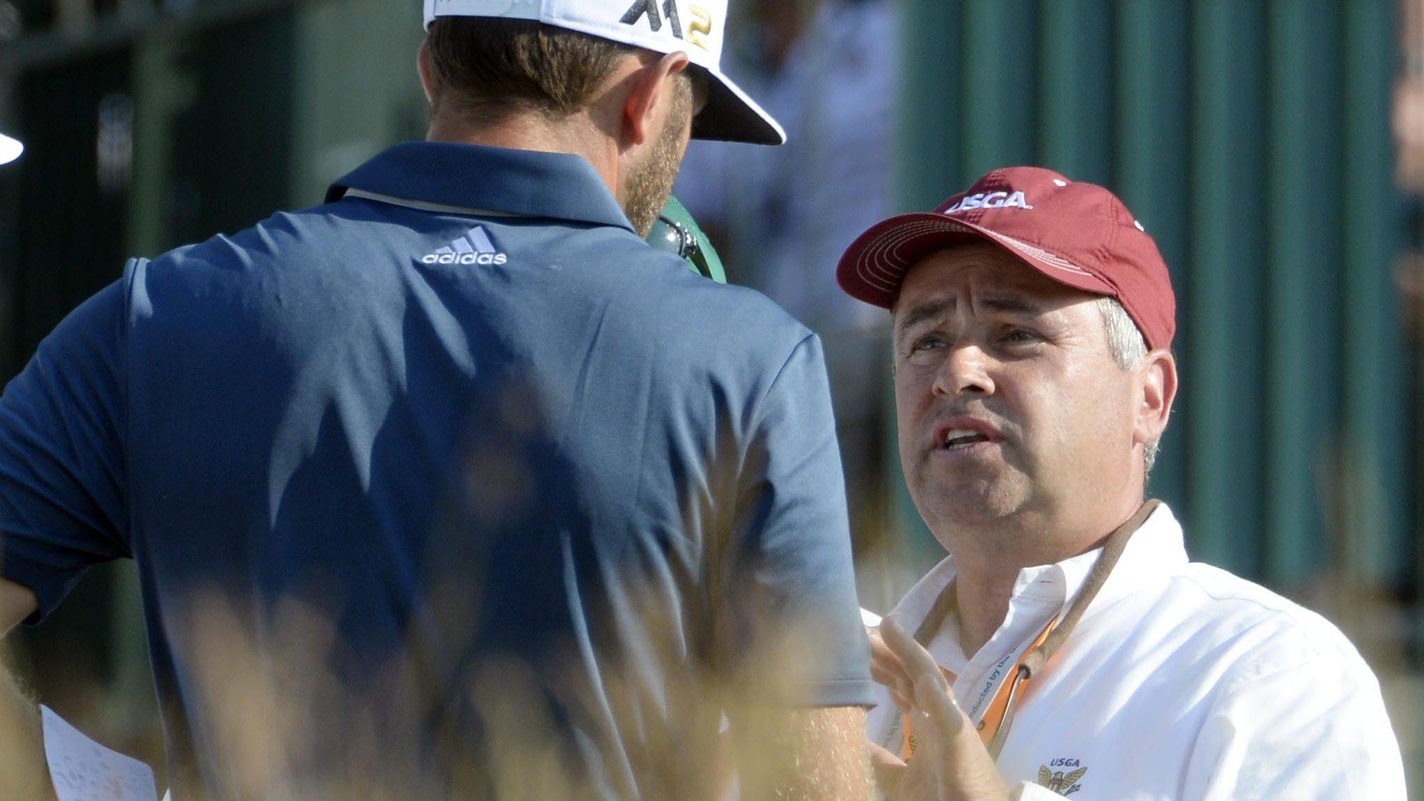 Dustin Johnson is spoken to by a course official