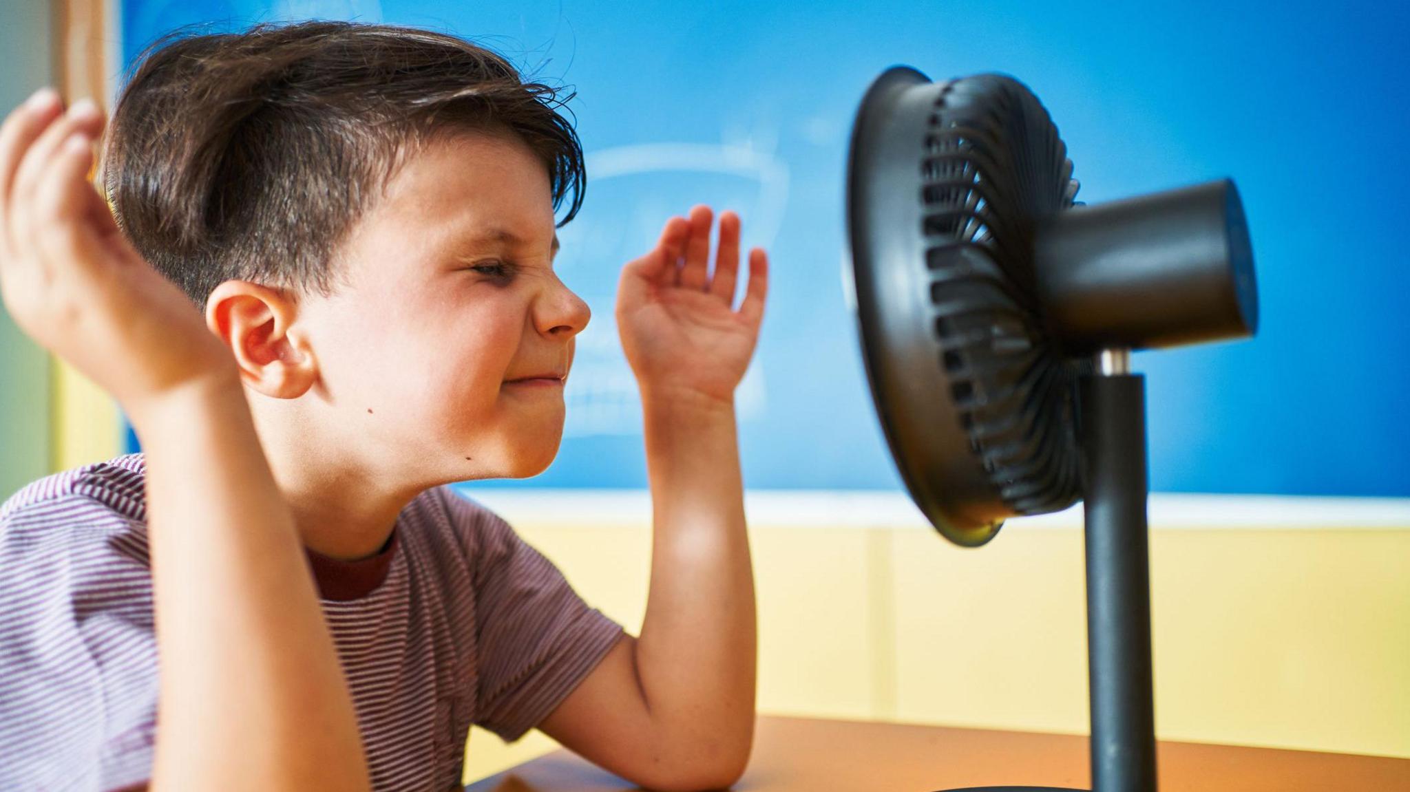 Boy sitting in front of fan.