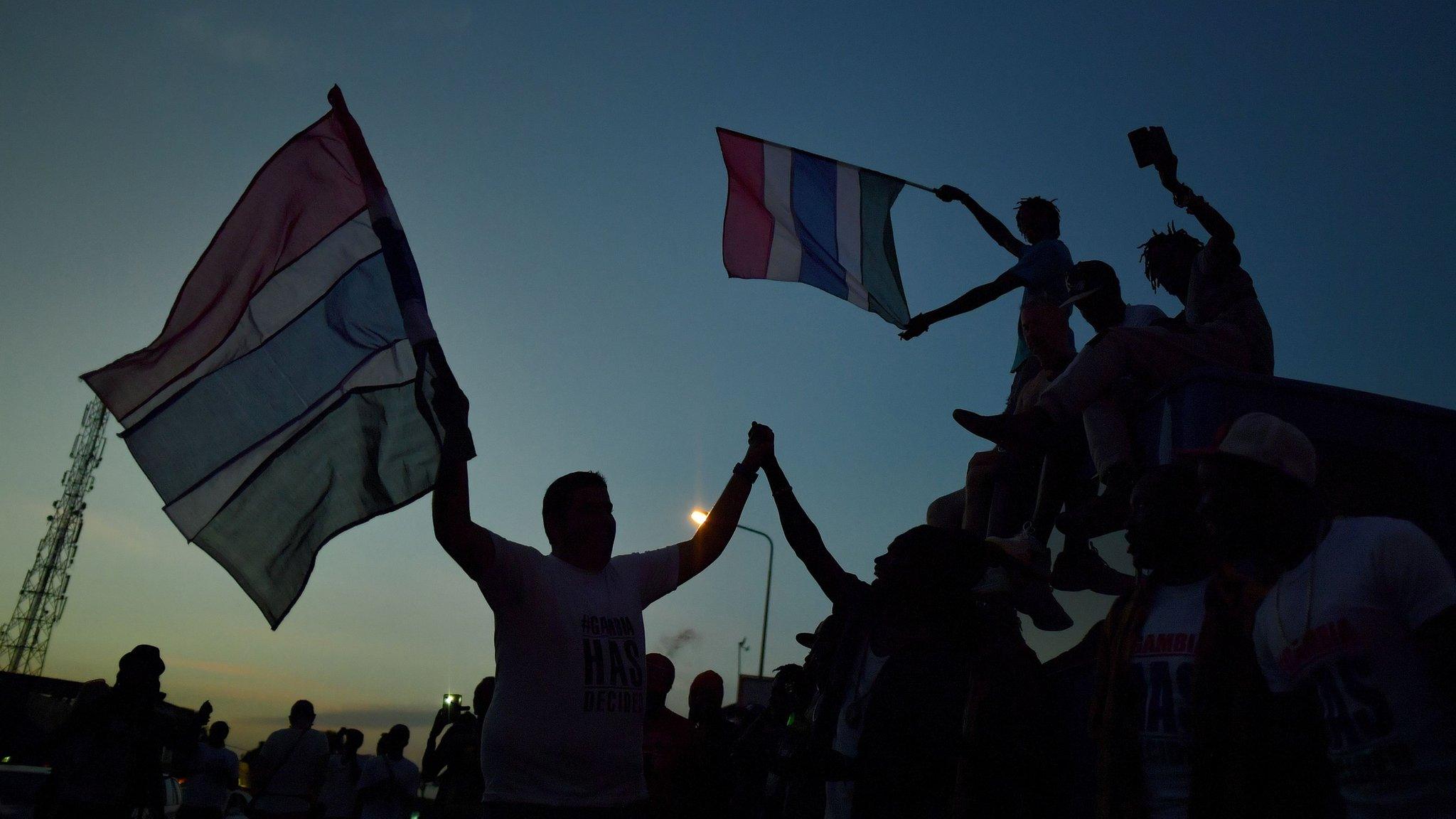 People celebrate in the streets with Gambian flags as they hear of the imminent departure of former Gambian leader Yahya Jammeh in Banjul on 21 January