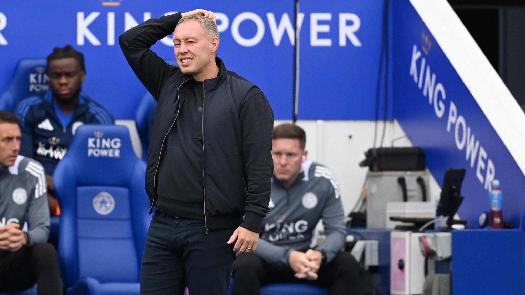 Steve Cooper, standing in front of the Leicester dugout, puts his right hand on his head.