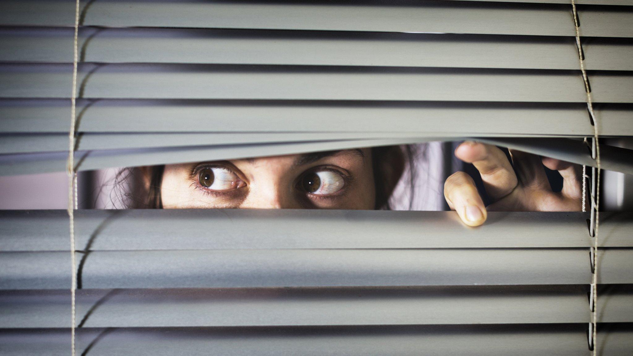 Woman looking through a blind