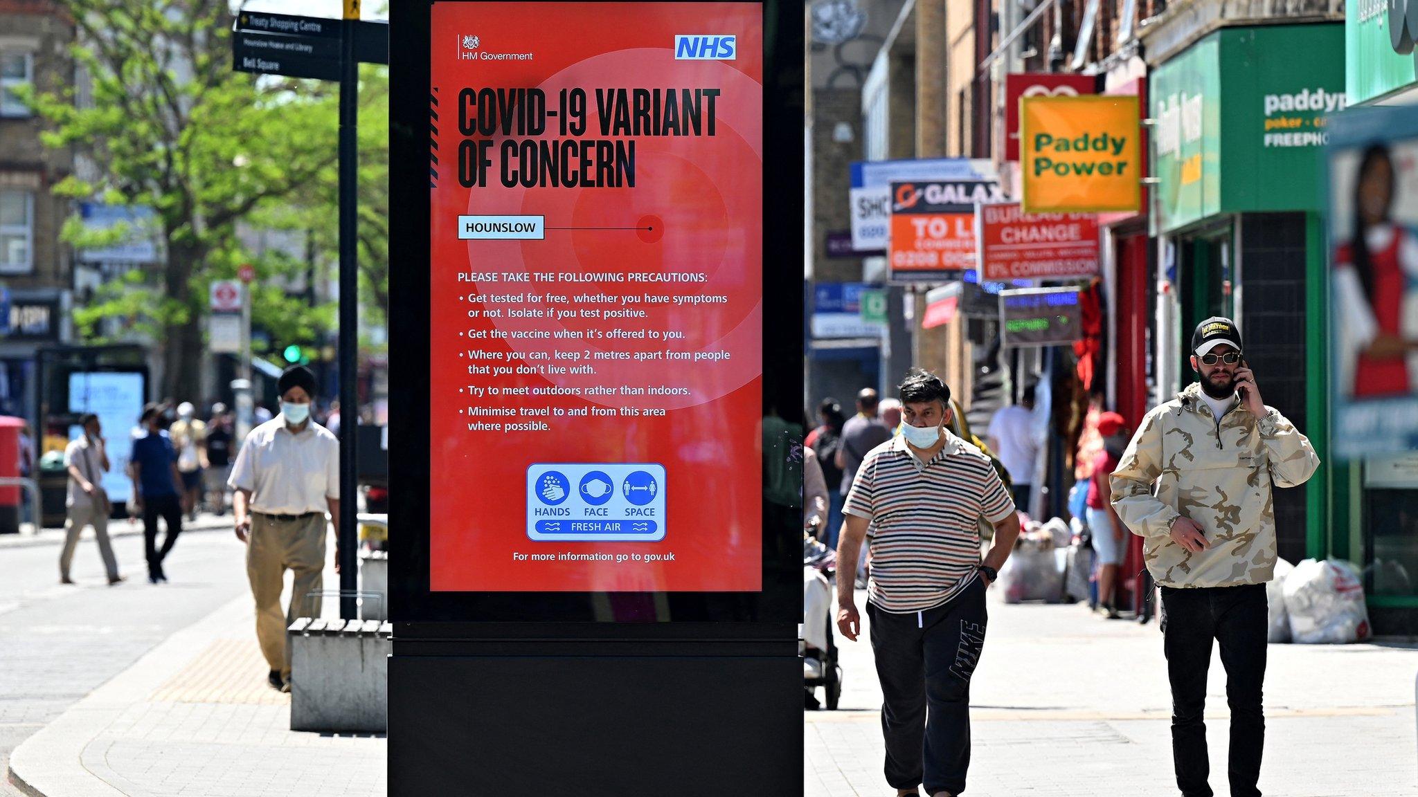 Pedestrians walk past a sign warning members of the public about the spread of Coronavirus, as they walk along the street in Hounslow, west London