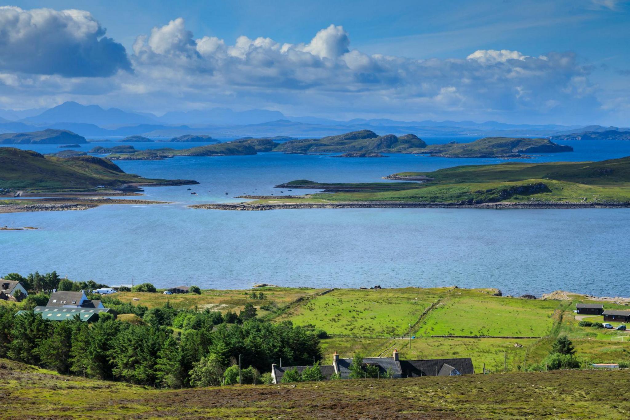 Landscape near Achiltibuie. There is a cluster of houses and the sea with the islands of the Summer Isles, and in the distance are hills and mountains.