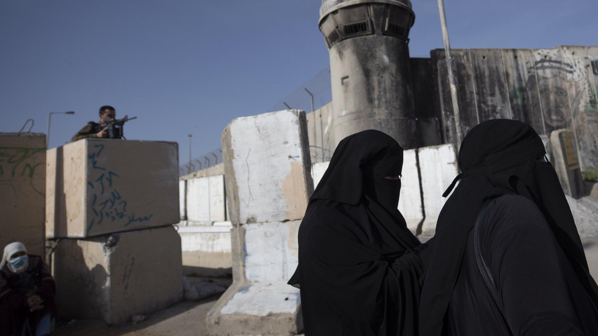 An Israeli soldier watches as Palestinians women wait to cross Qalandia checkpoint to attend the first Friday prayer service of Ramadan at the al-Aqsa Mosque in occupied East Jerusalem (16 April 2021)