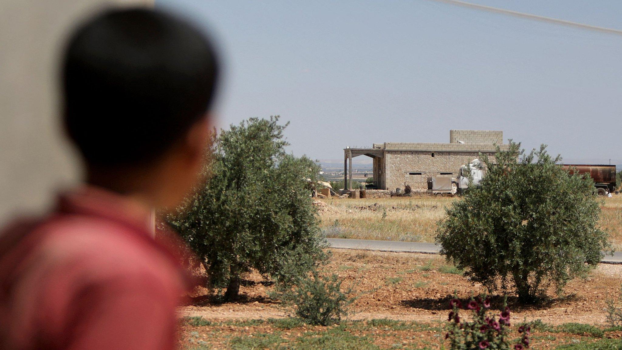 A boy looks at a house in the village of al-Hamira, northern Syria, that was reportedly targeted in a raid by US-led coalition forces that led to the capture of a senior IS leader (16 June 2022)