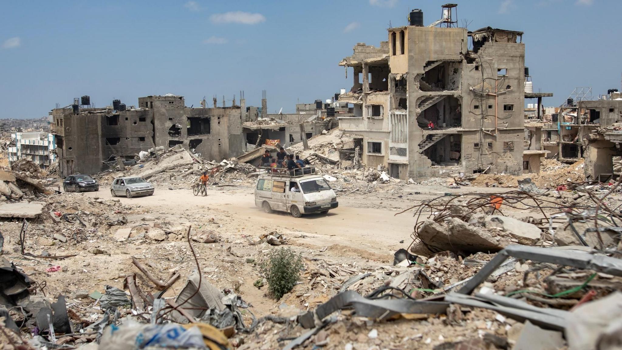 Palestinians walk and drive past buildings destroyed during a recent Israeli ground operation in the southern Gaza city of Khan Younis (7 April 2024)