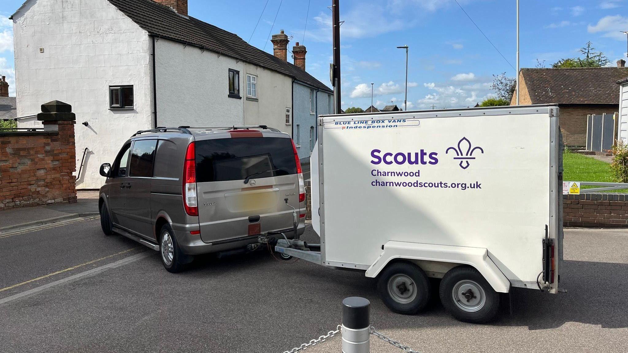 A box trailer with the words 'Scouts Charnwood' printed on the side, being towed by a small van