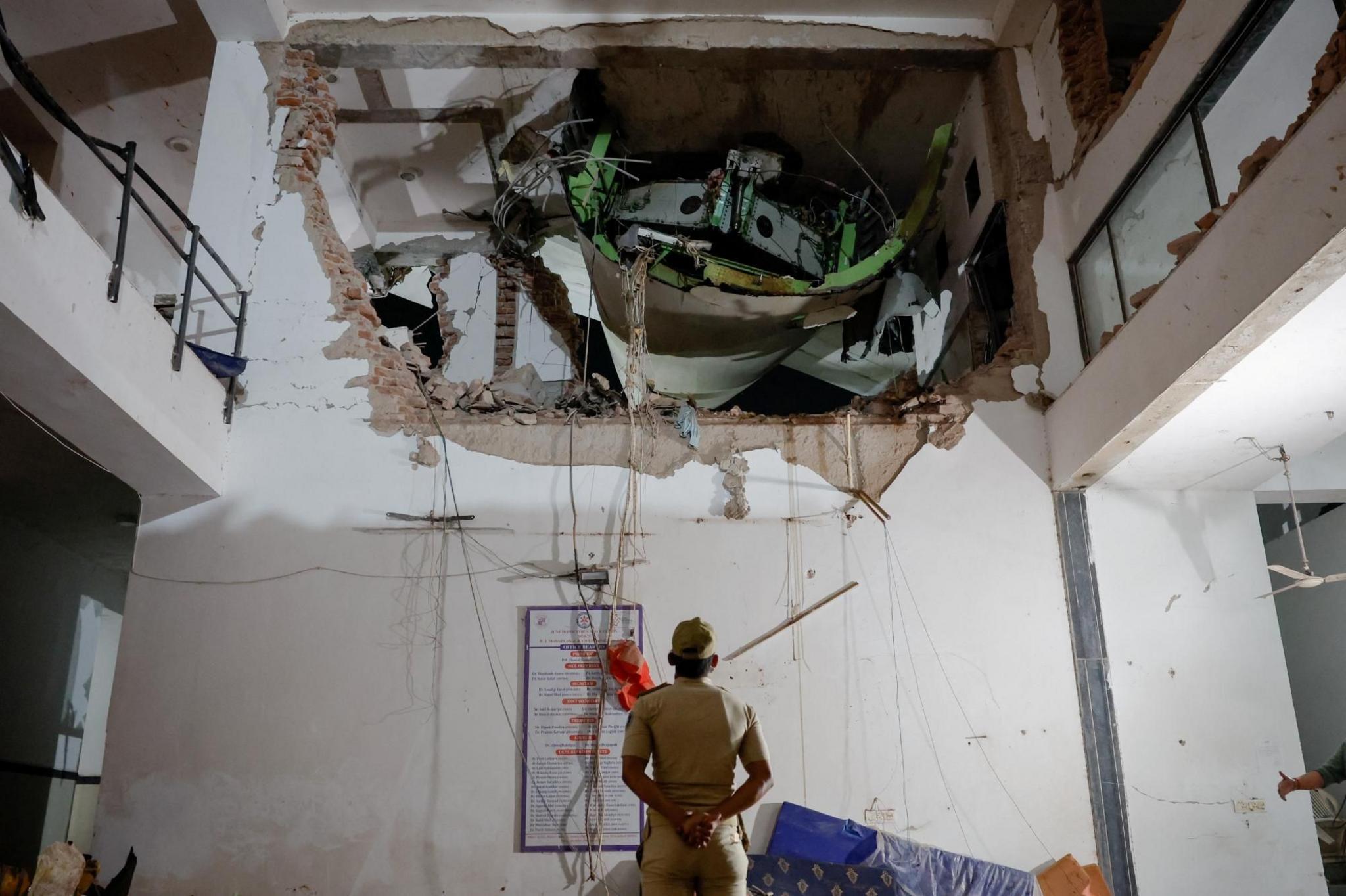 A police officer stands in front of debris at the crash site. He is inside a building and there is an enormous hole in the wall, where part of the plane can be seen.