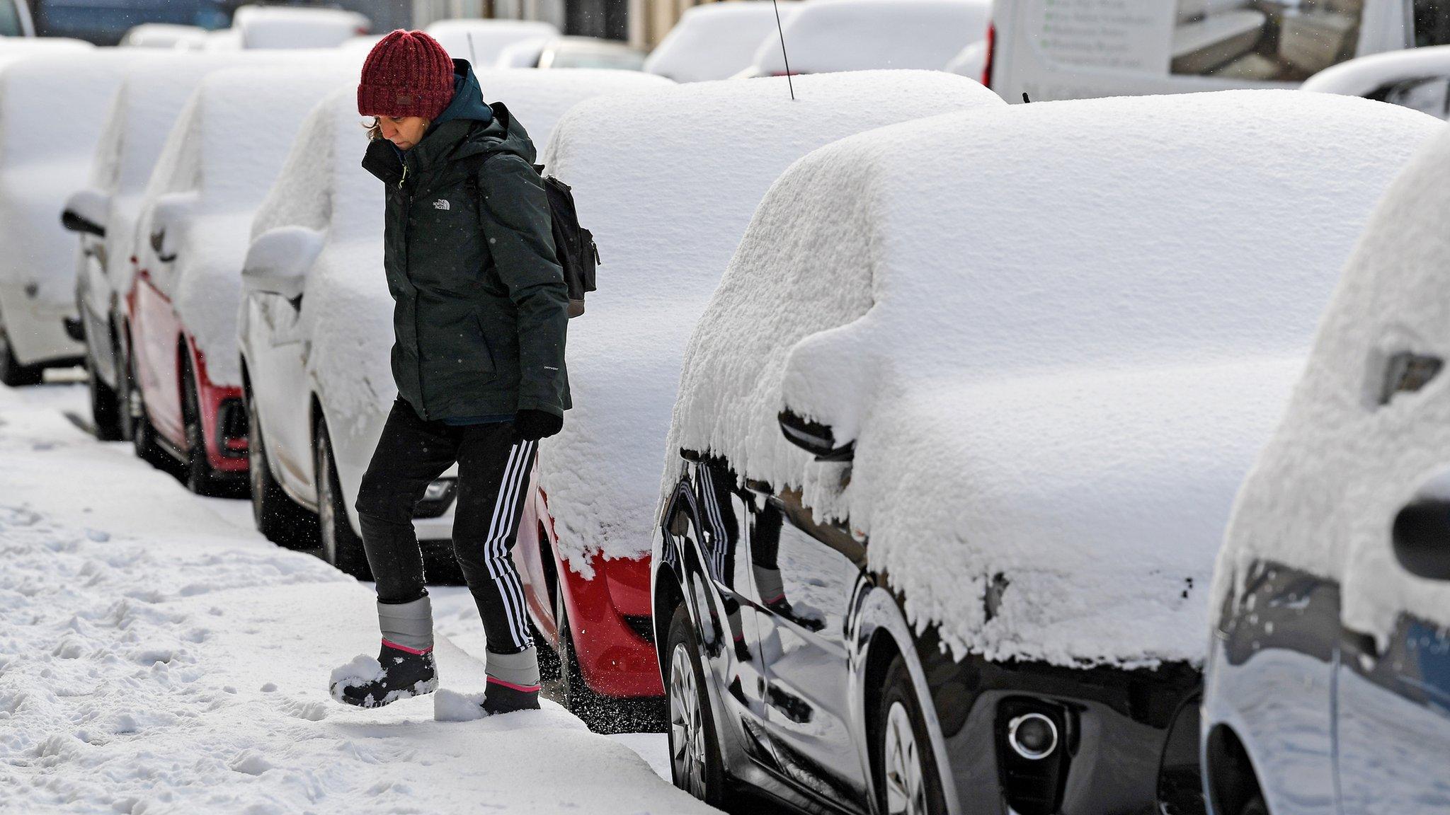 woman walks between snowy cars