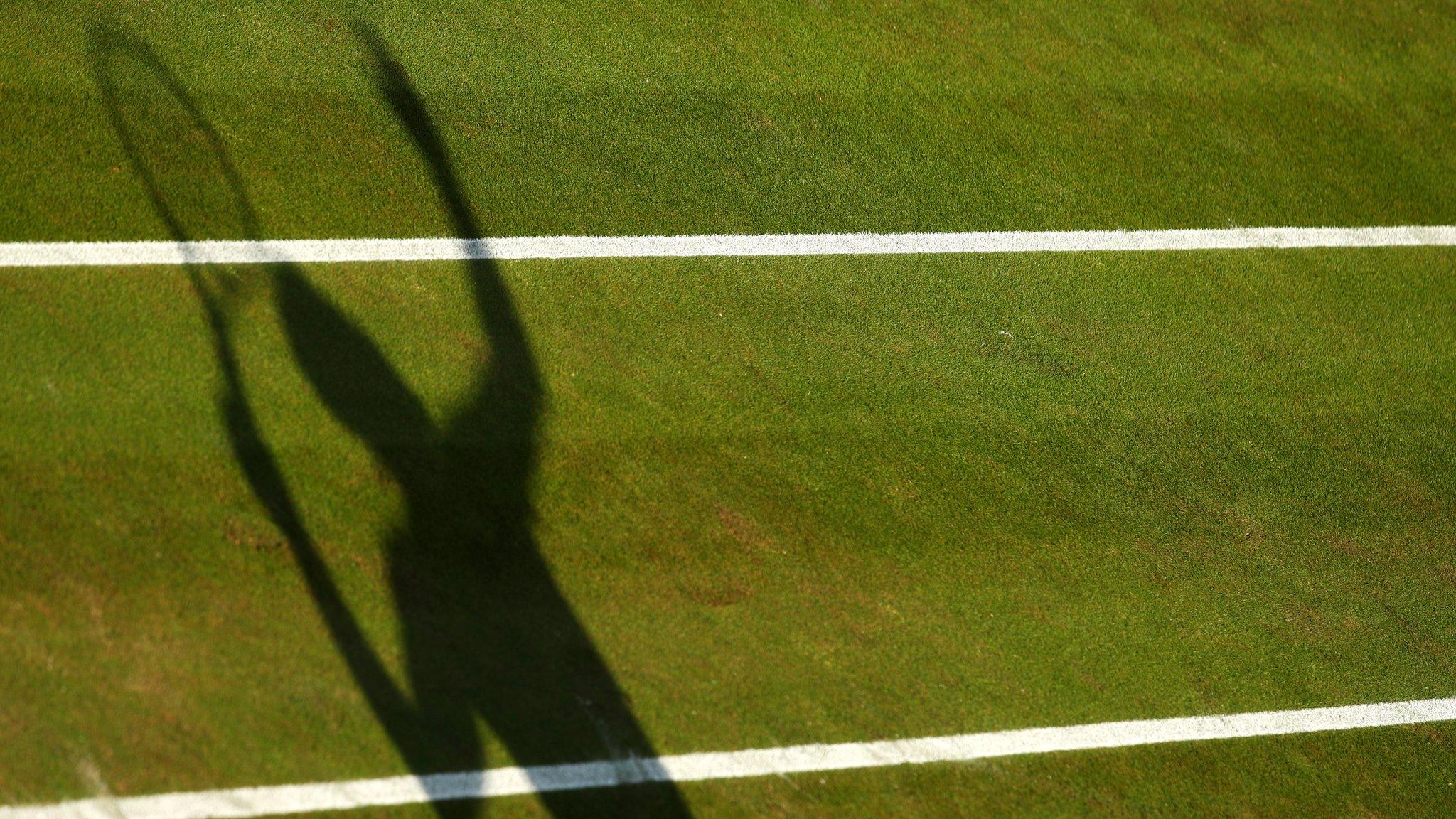 A shadow of a tennis player serving on a grass court