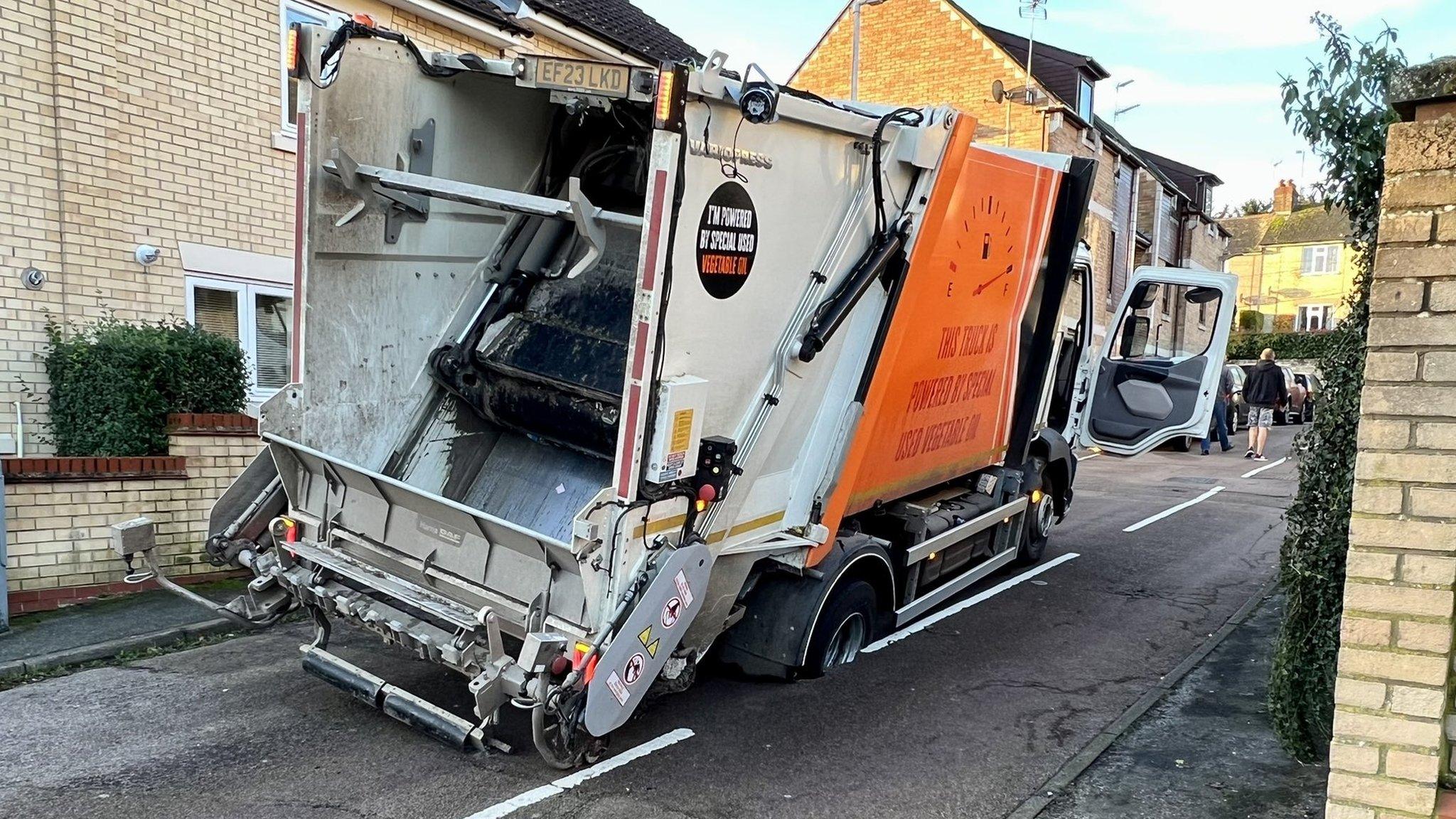 A bin lorry stuck in a hole in the road