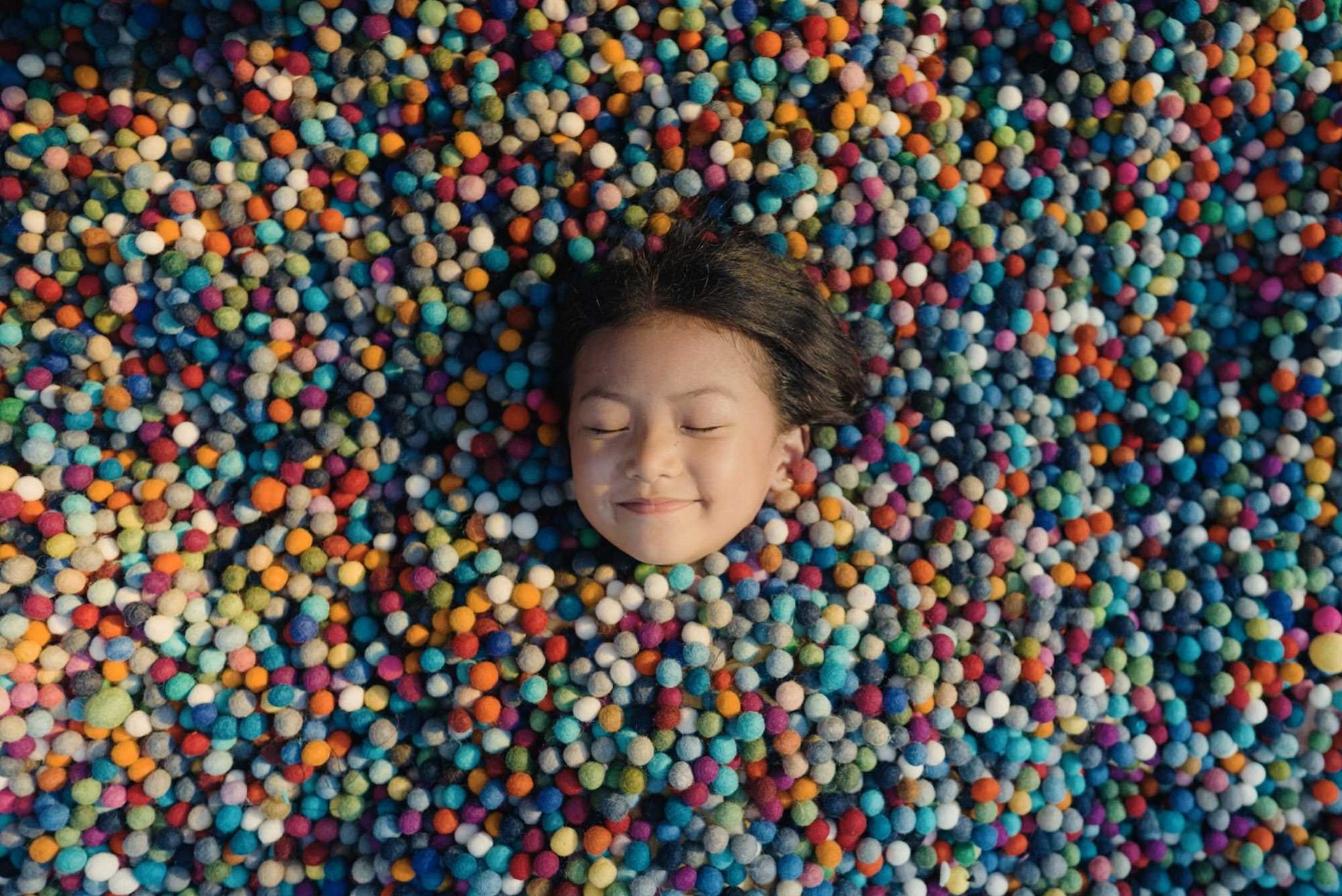 Little girl smiling with her eyes closed surrounded by small colourful felt balls.