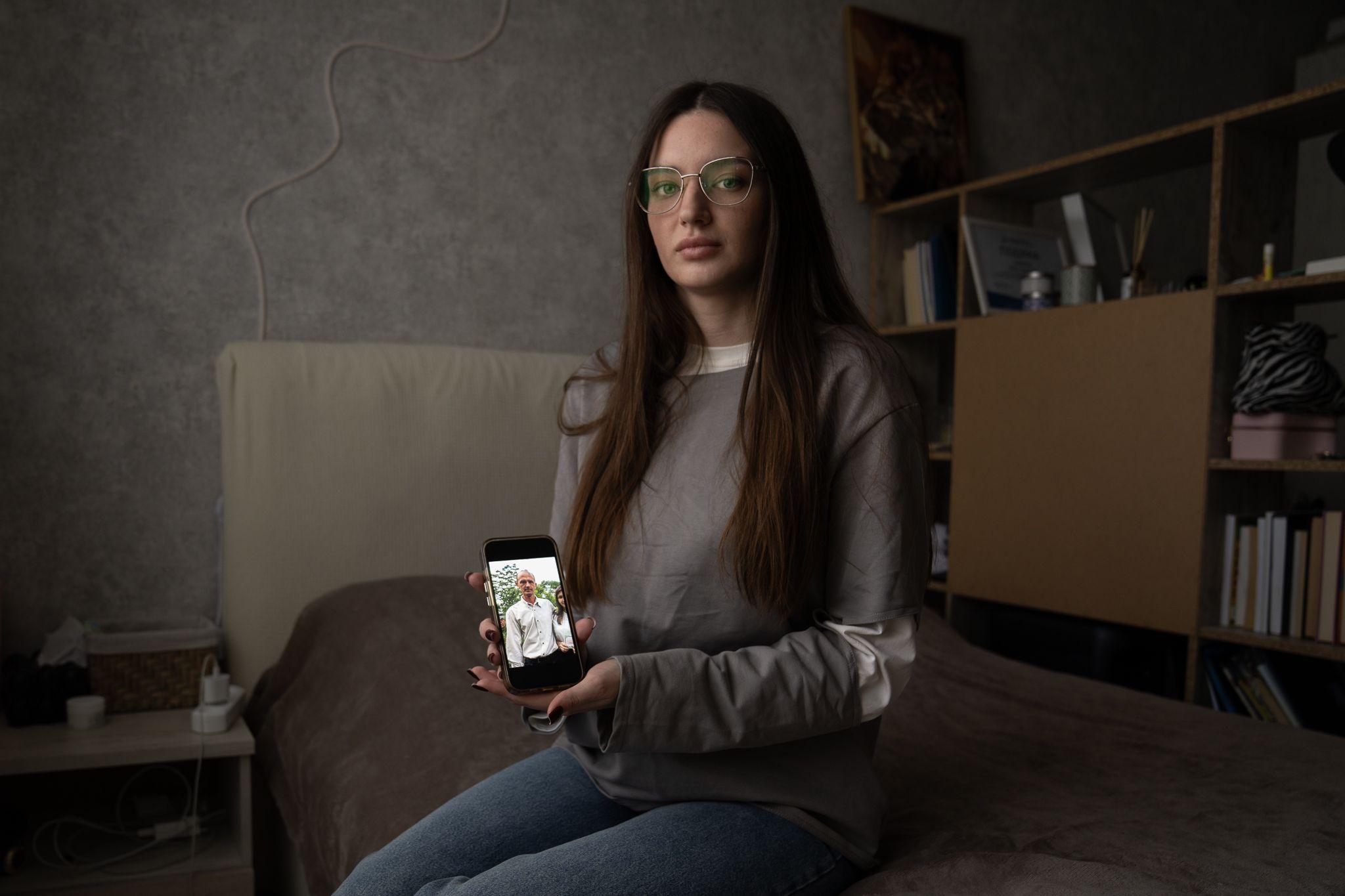 Yulia Hripun sitting in her bedroom with a picture of her captive father on her iPhone.