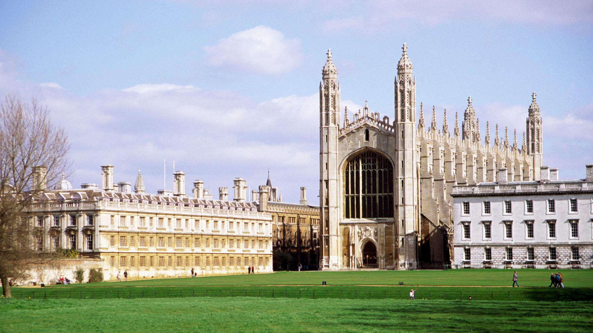 King's College, a grand-looking stone building with spires and stained glass, photographed from across a stretch of grass on a sunny day.