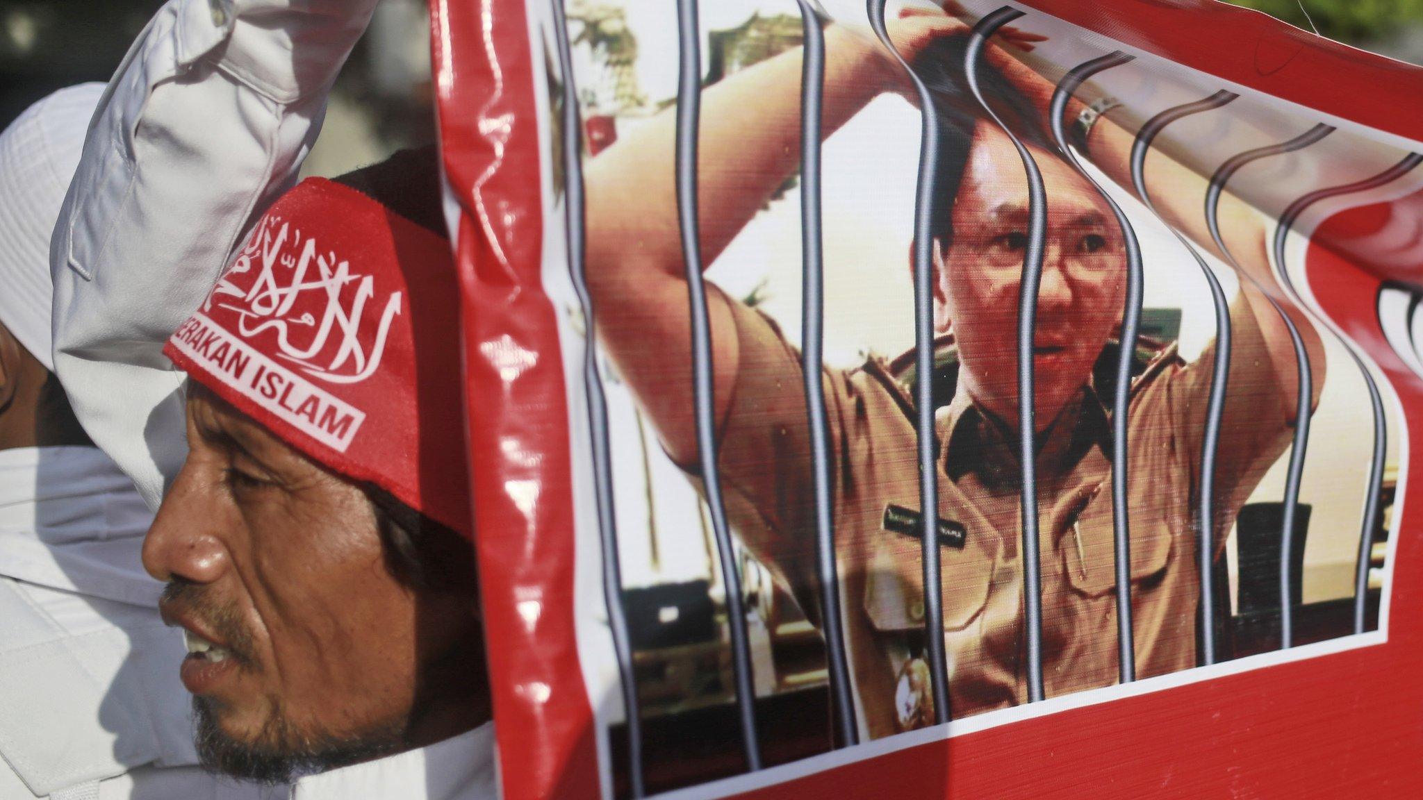 A Muslim protester holds a banner with picture depicting Jakarta Governor Basuki Tjahaja Purnama, popularly known as "Ahok," behind bars during a rally outside the court where his trial hearing of is held in Jakarta, Indonesia, on 20 December 2016