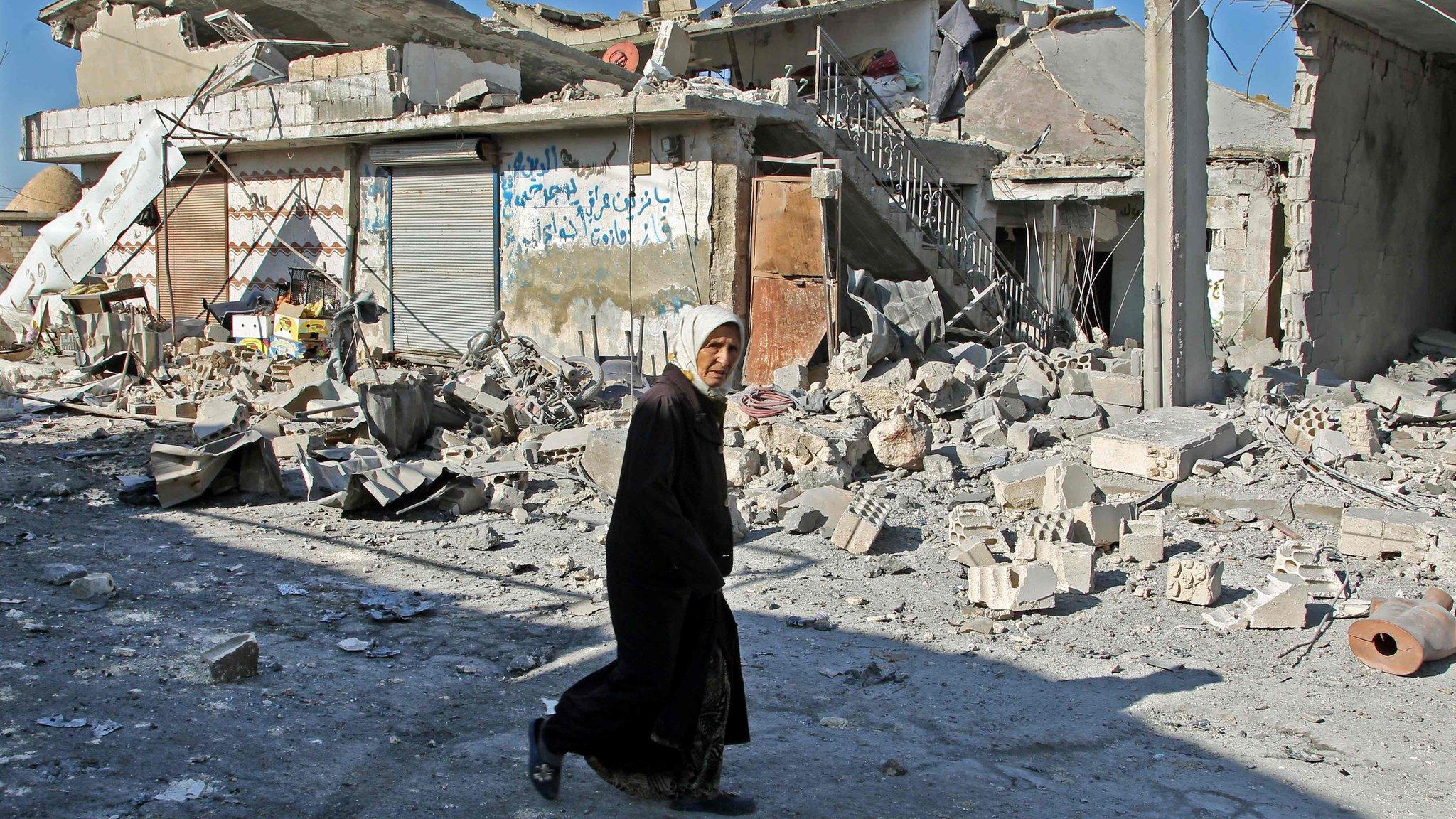 A Syrian woman walks past buildings destroyed in a reported government air strike in the town of Maasaran in Idlib province (17 December 2019)