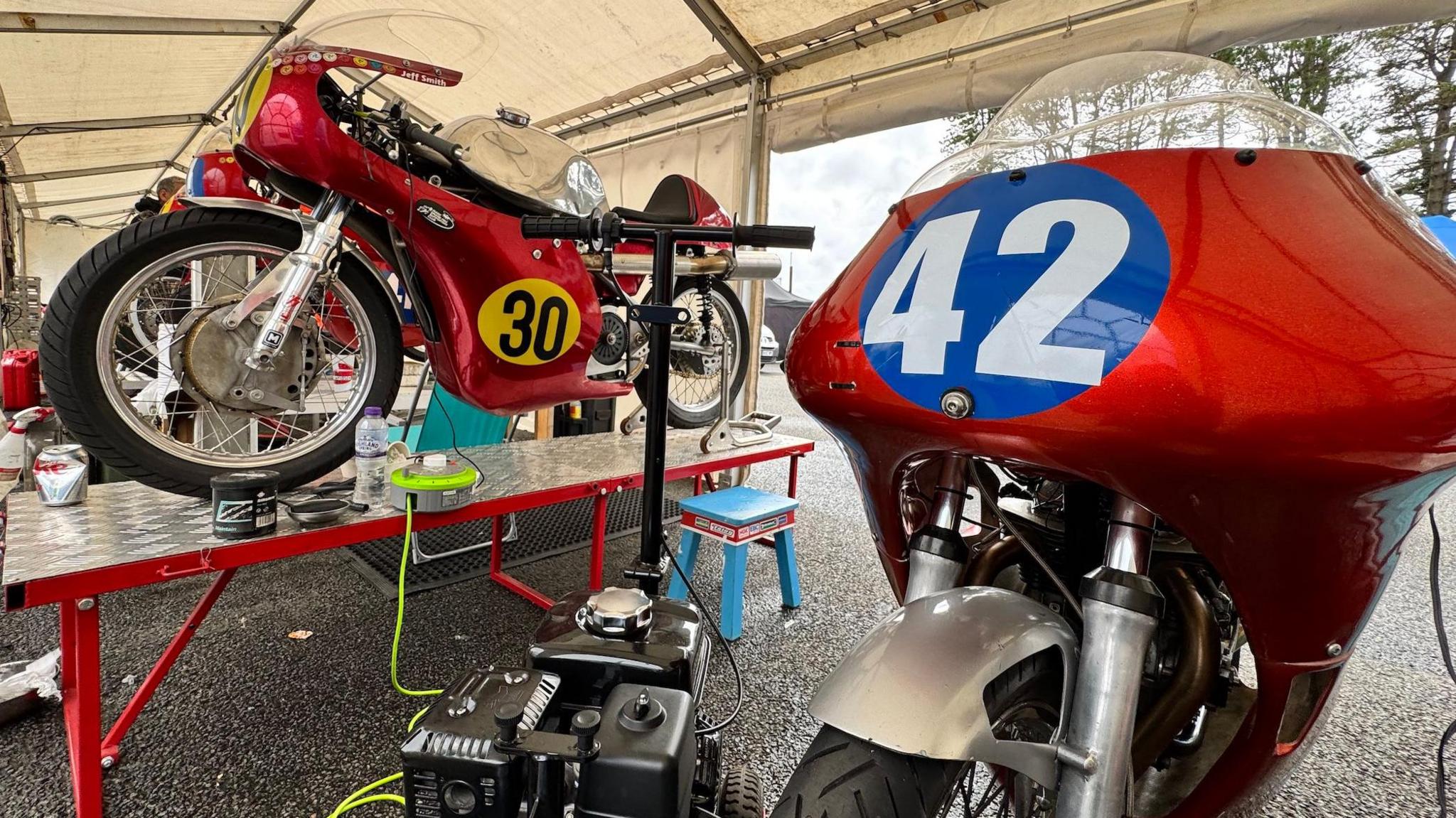 The 350 Honda and 500 Matchless machines, both in red, numbered 42 (right) and 30, inside a white tent.