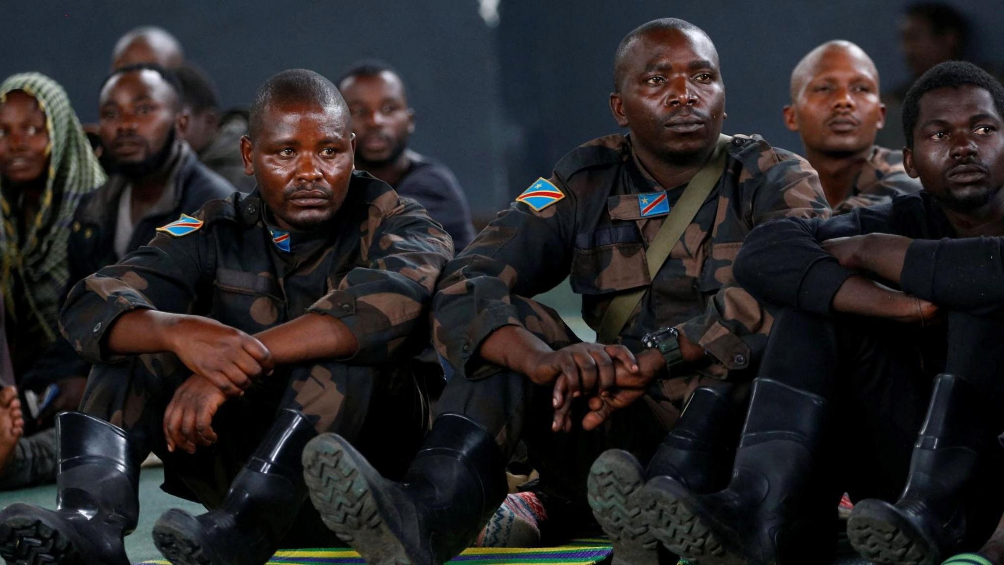 Congolese soldiers, most in fatigues and gum boots, sit on the floor in a room in Rwanda, where they went after surrendering in across the border in Goma in DR Congo