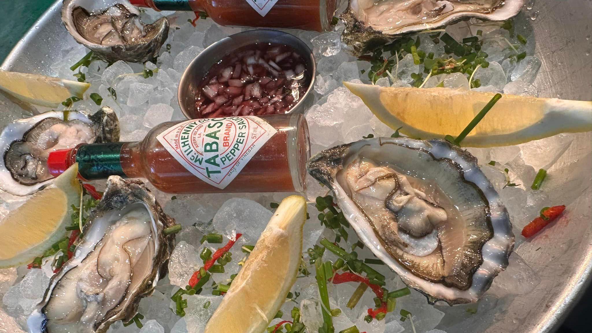 Oysters, tabasco and lemon slices in a metal dish full of ice 