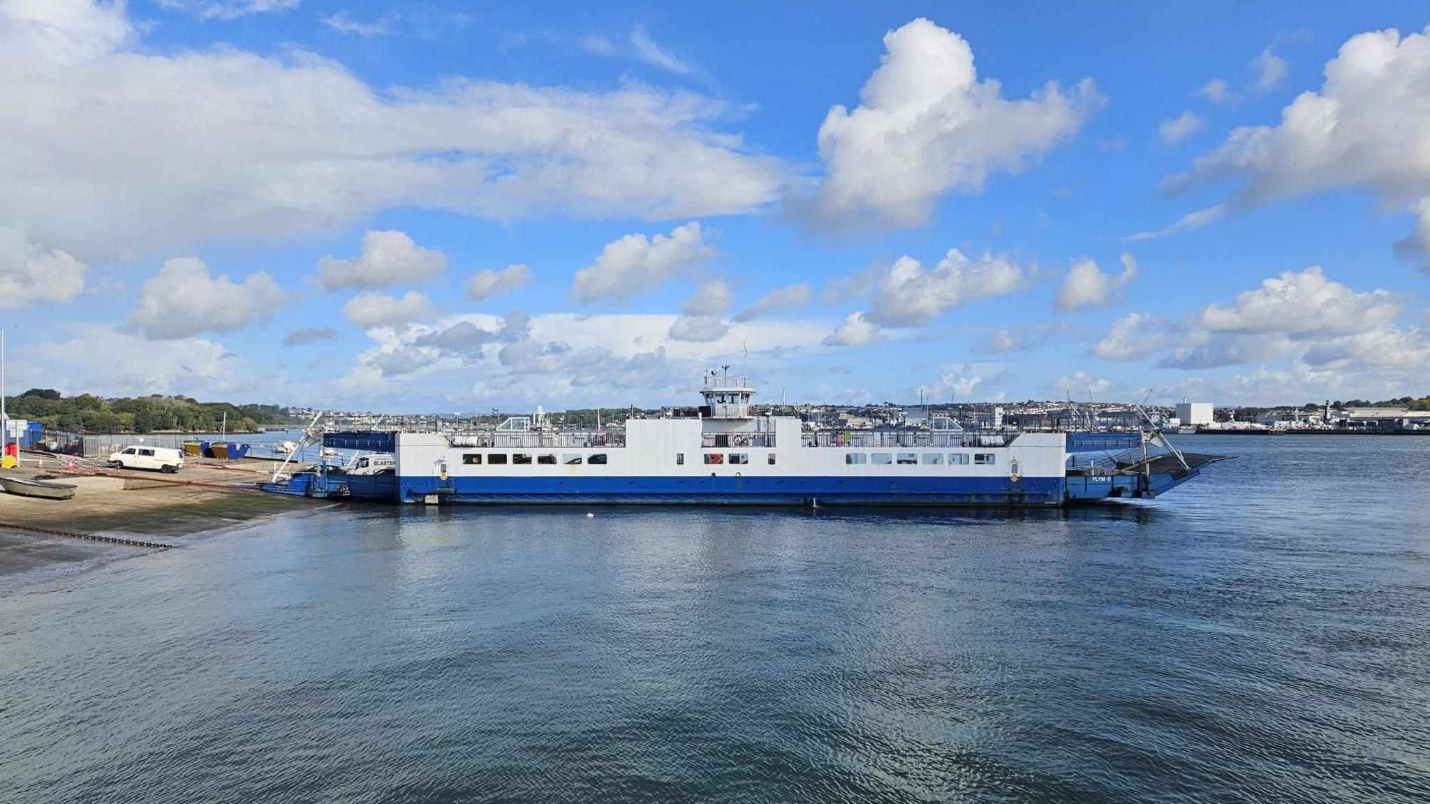The Torpoint Ferry has its ramp resting on the shore. The sea is calm and it's a sunny day.
