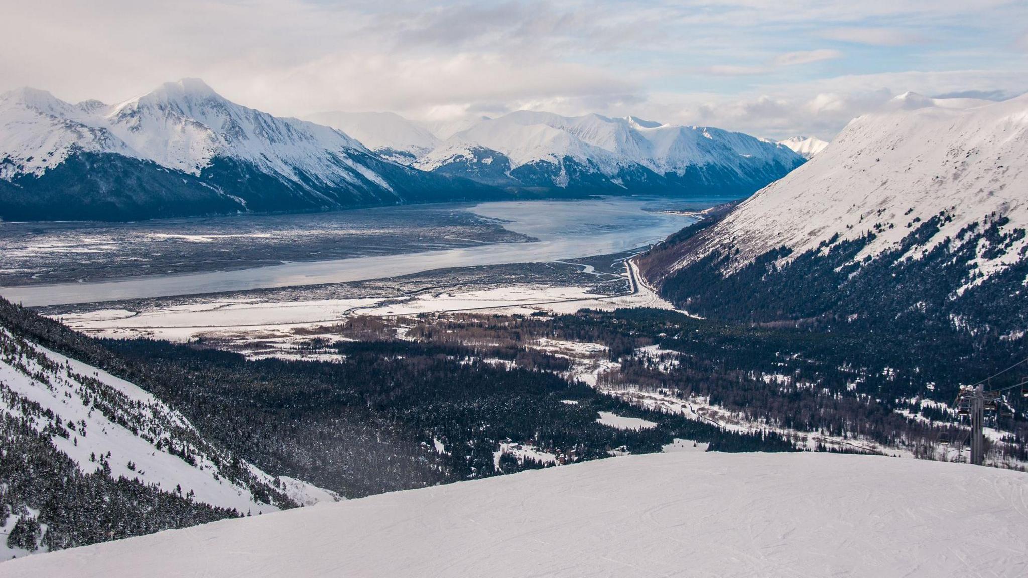 Looking down on Girdwood from Alyeska ski resort. There are large snowy mountains and green trees in the valley