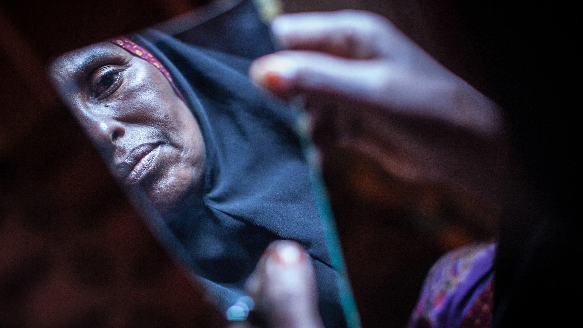 A woman who carries out FGM reflected in a broken piece of mirror