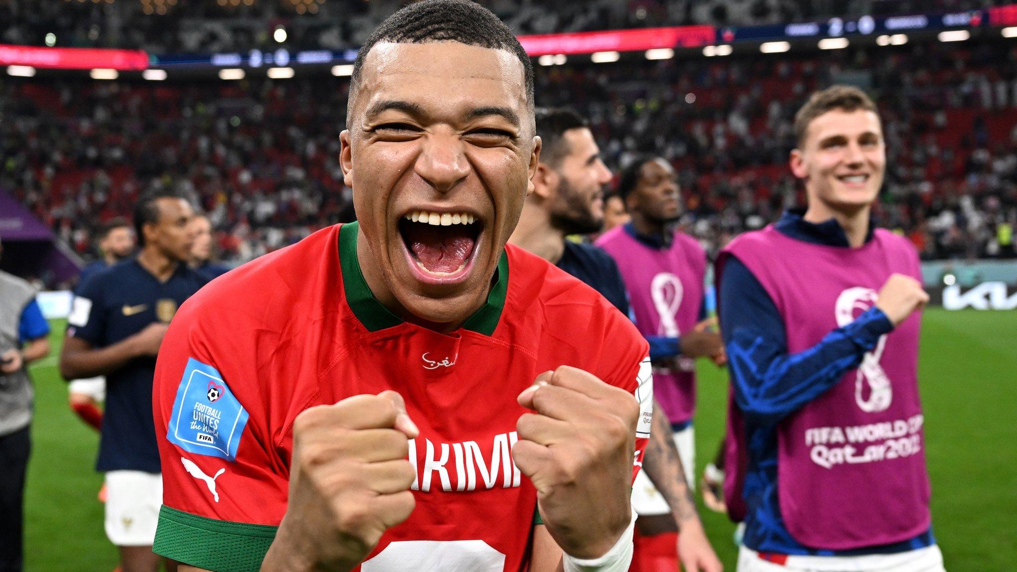 A close-up shot of Kylian Mbappe shouting at the camera in celebration while wearing Achraf Hakimi's Morocco shirt back to front