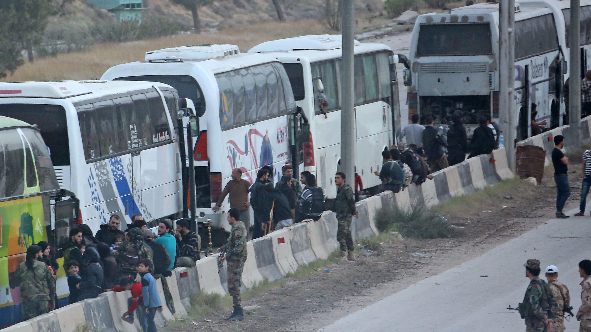 Buses wait to transport Syrian rebel fighters and their families from the town of Harasta, in the Eastern Ghouta, to Idlib province (22 March 2018)