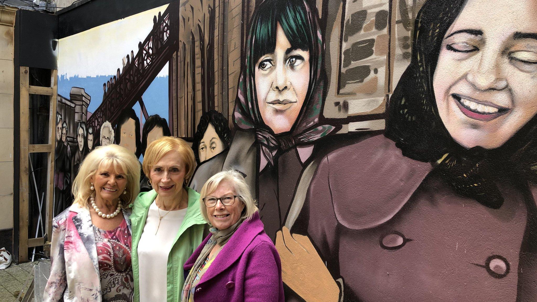 factory girls standing with mural