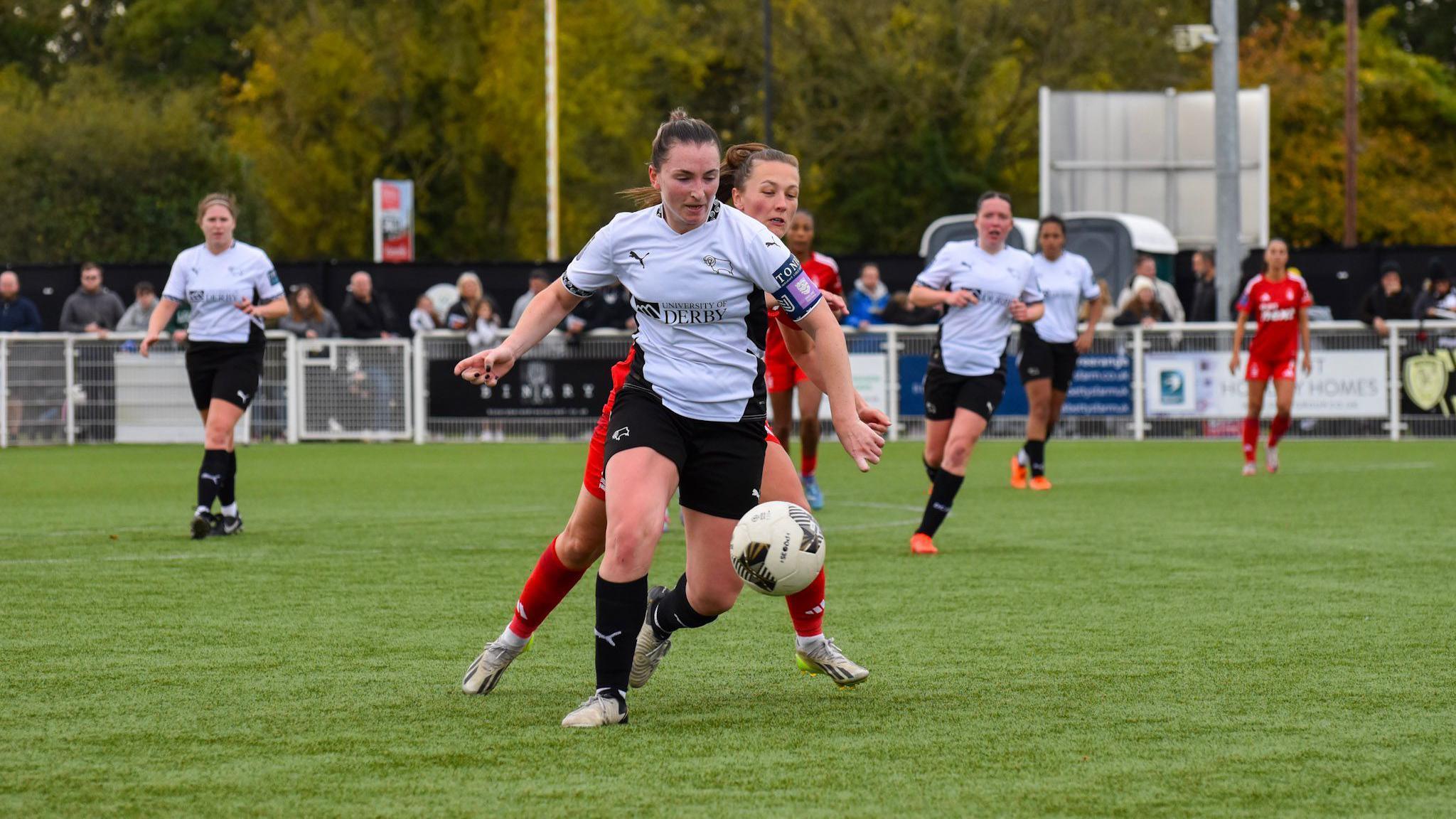 Derby women's captain Emily Joyce on a football pitch chasing a ball, surrounded by other players