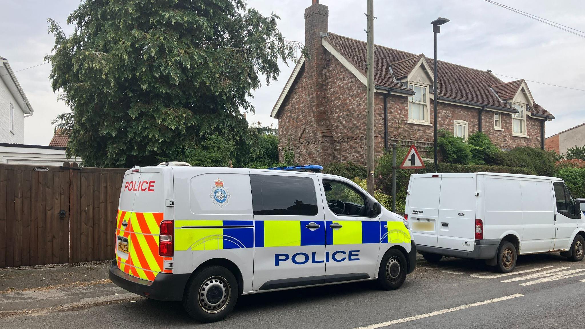 A police van parked at the side of a road behind a white transit van.