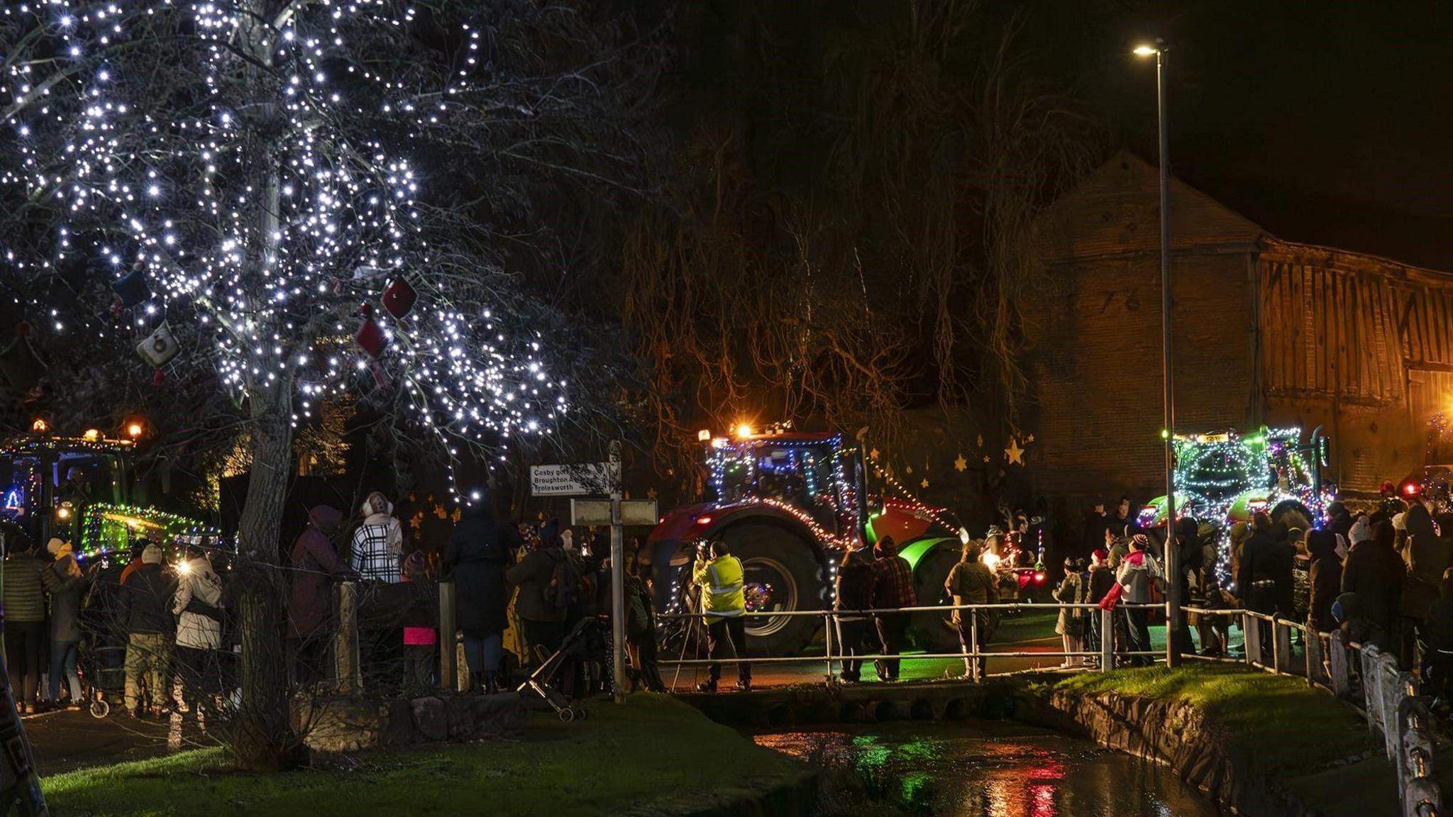 Crowds of people watch on as the tractor run drives through a village.