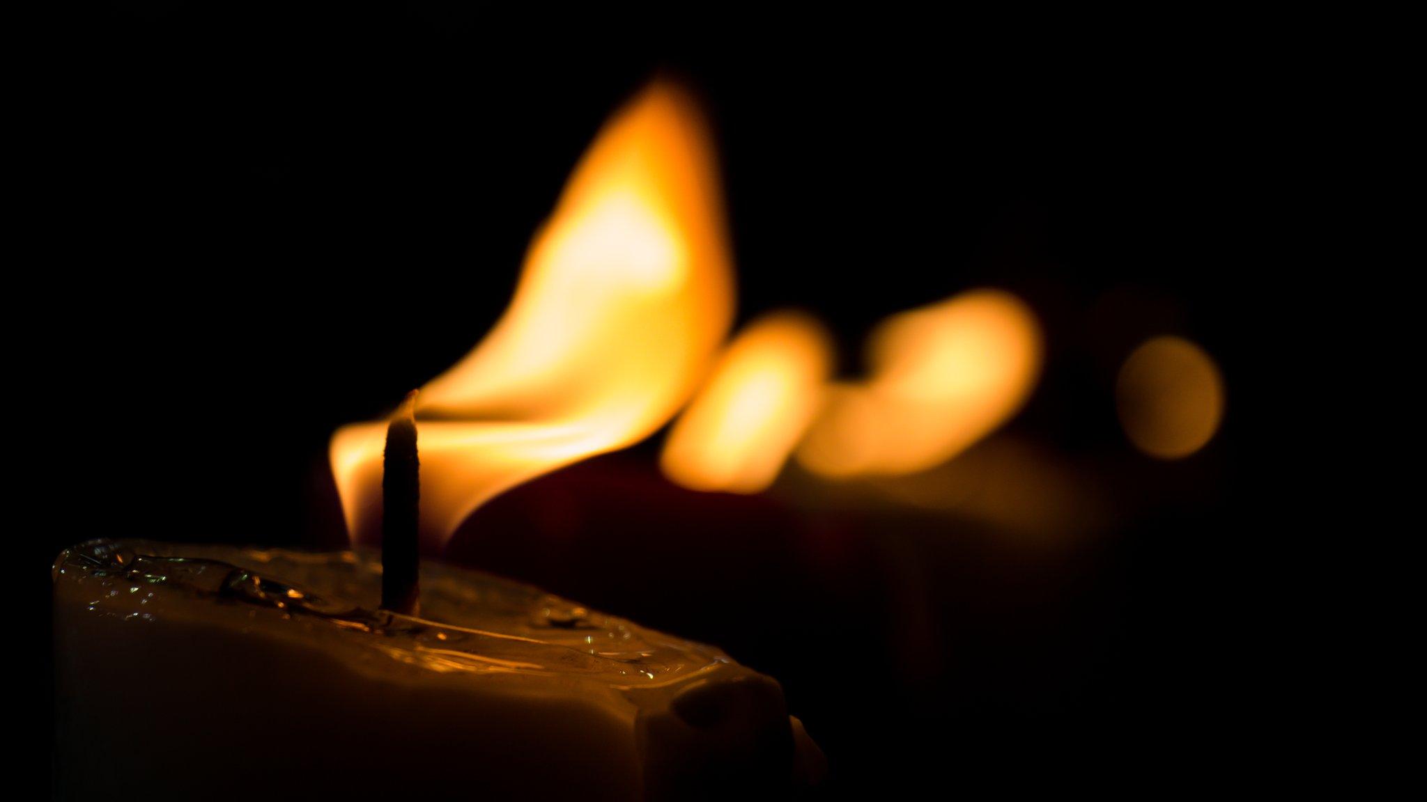 Image shows a lit candle burning in the dark