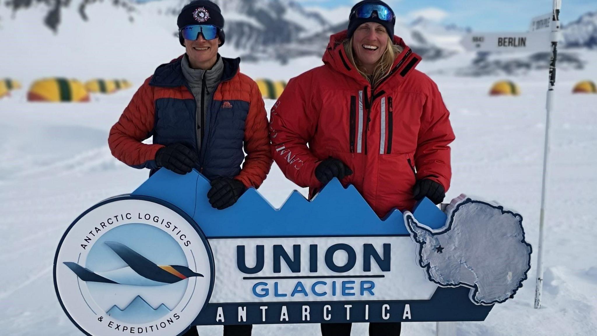 The Antarctic Fire Angels smiling behind a sign which says Union Glacier, Antarctica