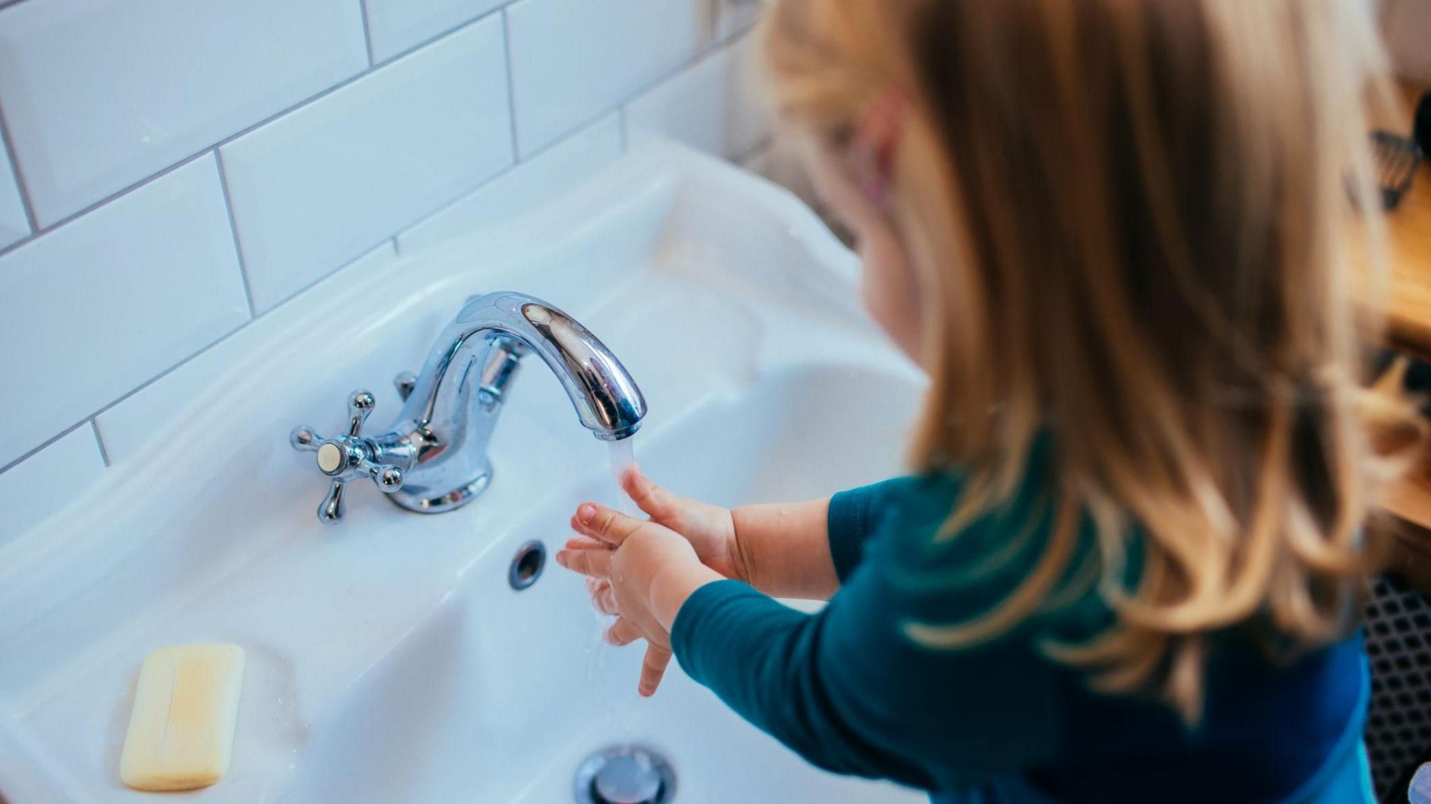 A young girl  with blonde hair washing her hands in the sink